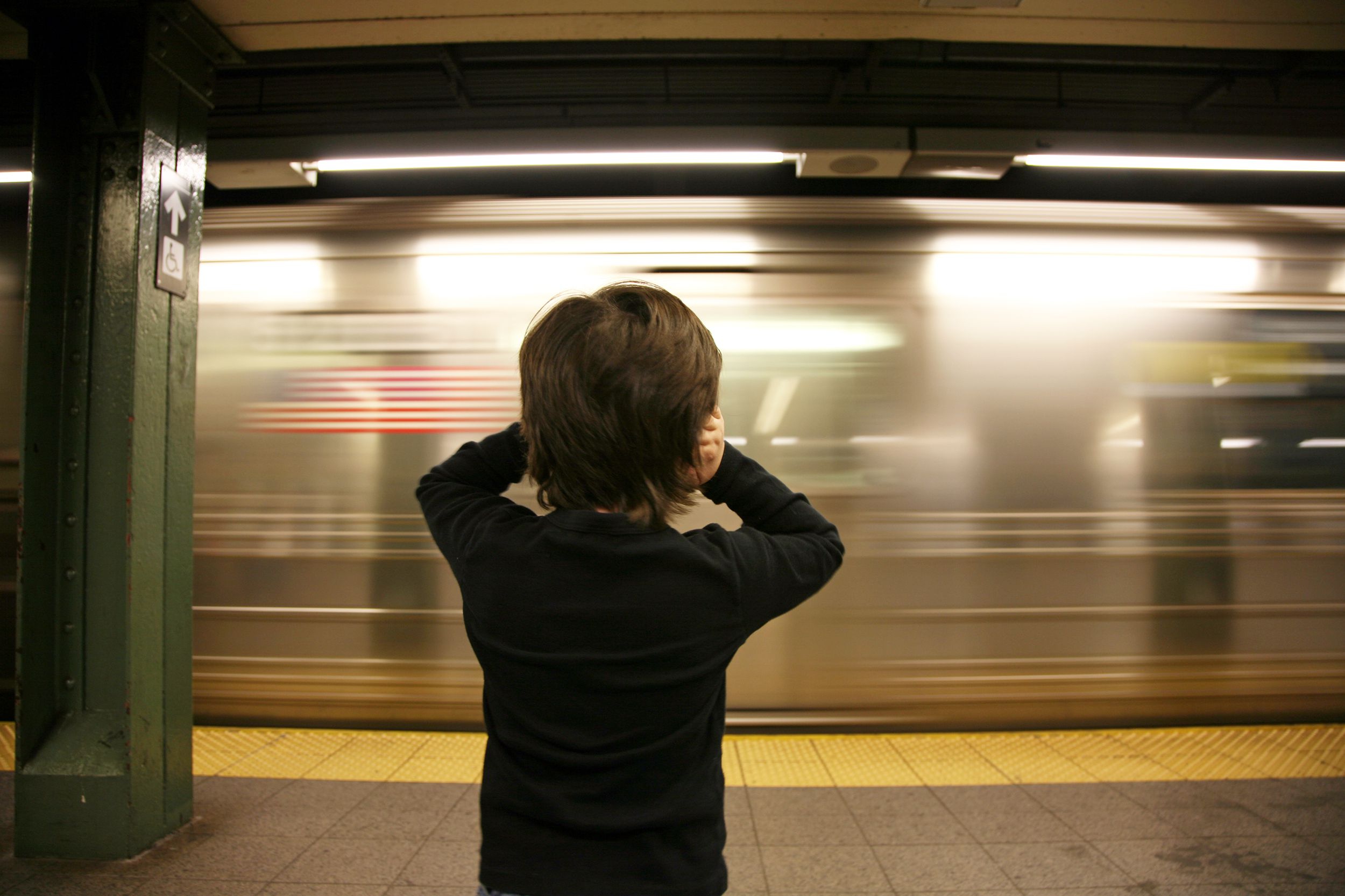 little child holding ears in face of nyc noisy nyc subway passing through station