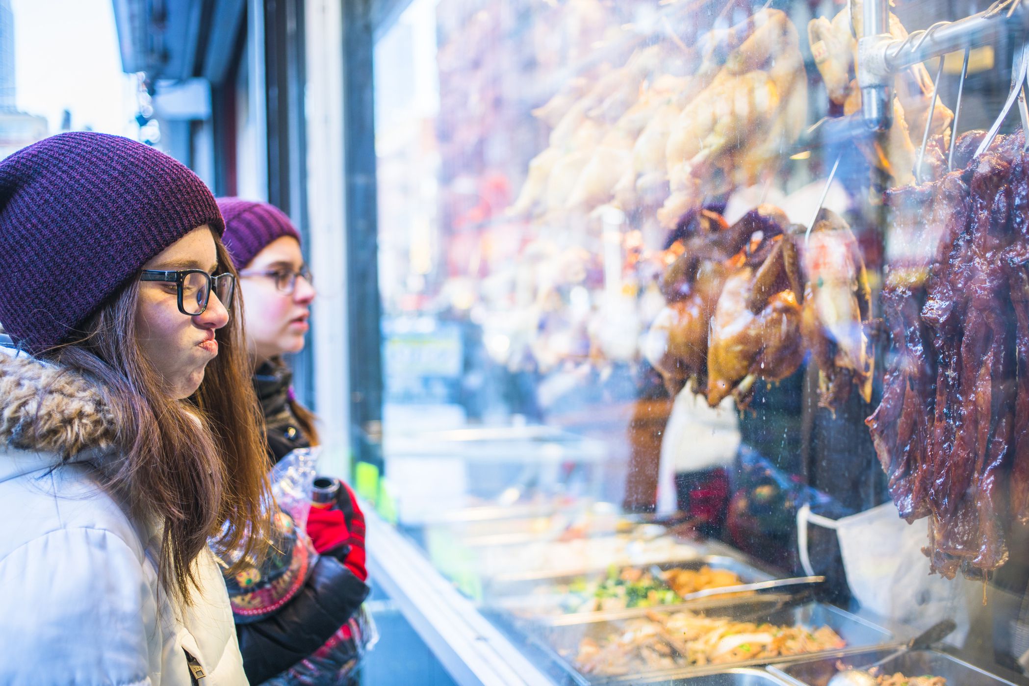 two young people looking skeptically at food in the window in chinatown