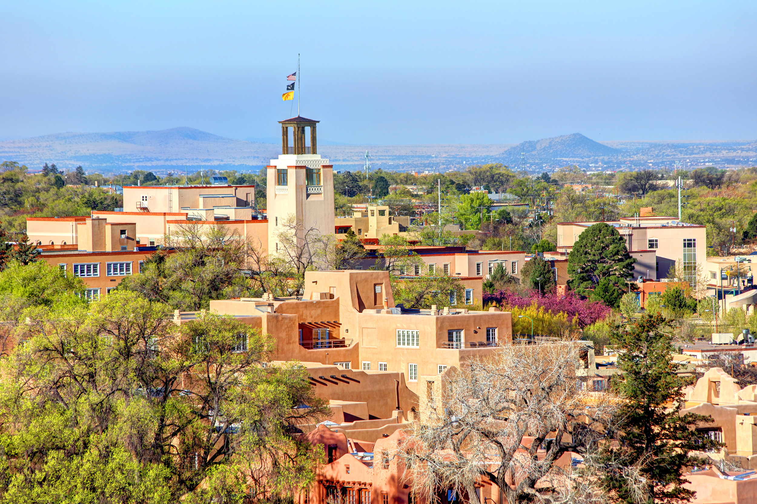 Aerial of buildings in downtown Santa Fe, New Mexico during a sunny day, focus on tops of buildings with two mountains in the background