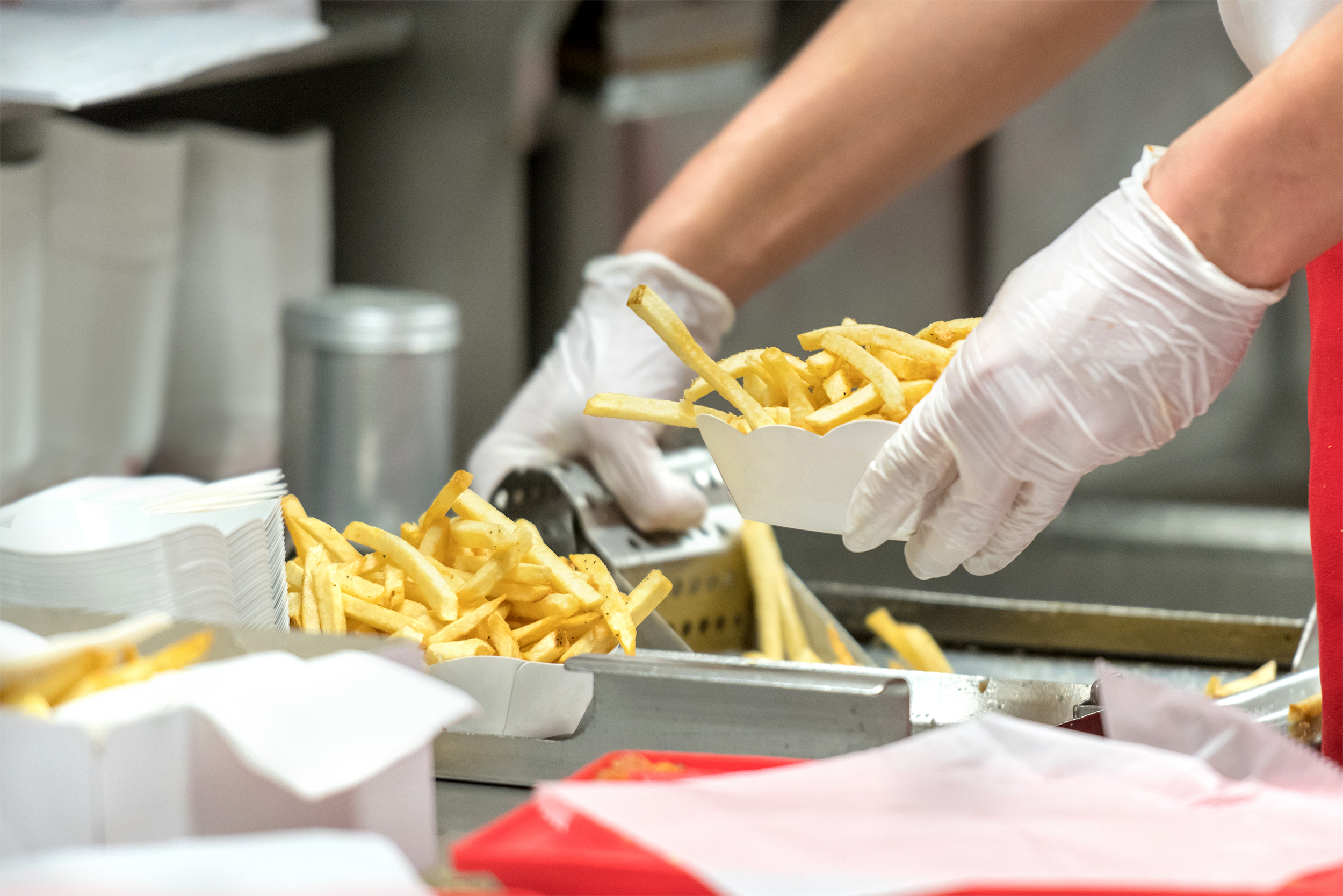 Hands scooping french fries in a fast food kitchen