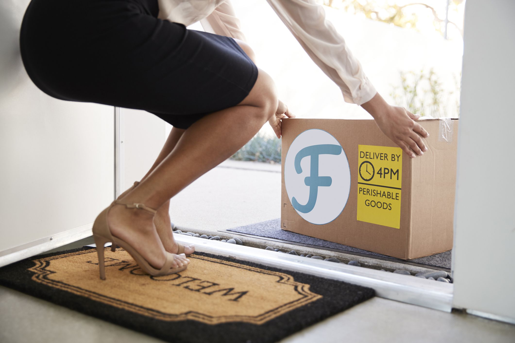 woman picking up box of fresh groceries on doorstep