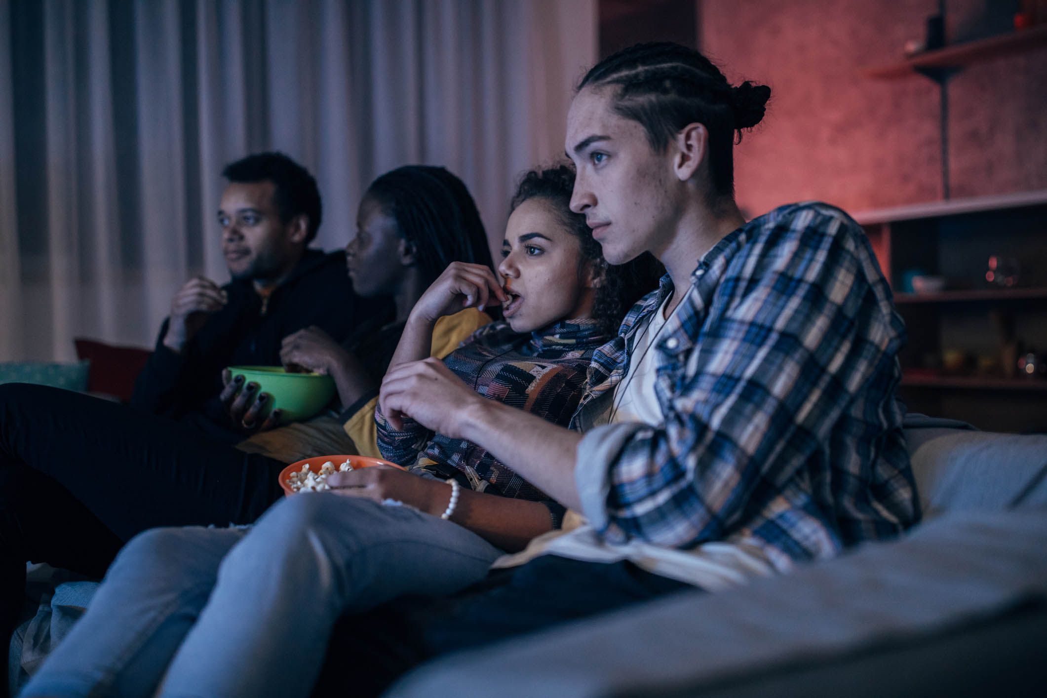 group of college students watching television on couch eating popcorn