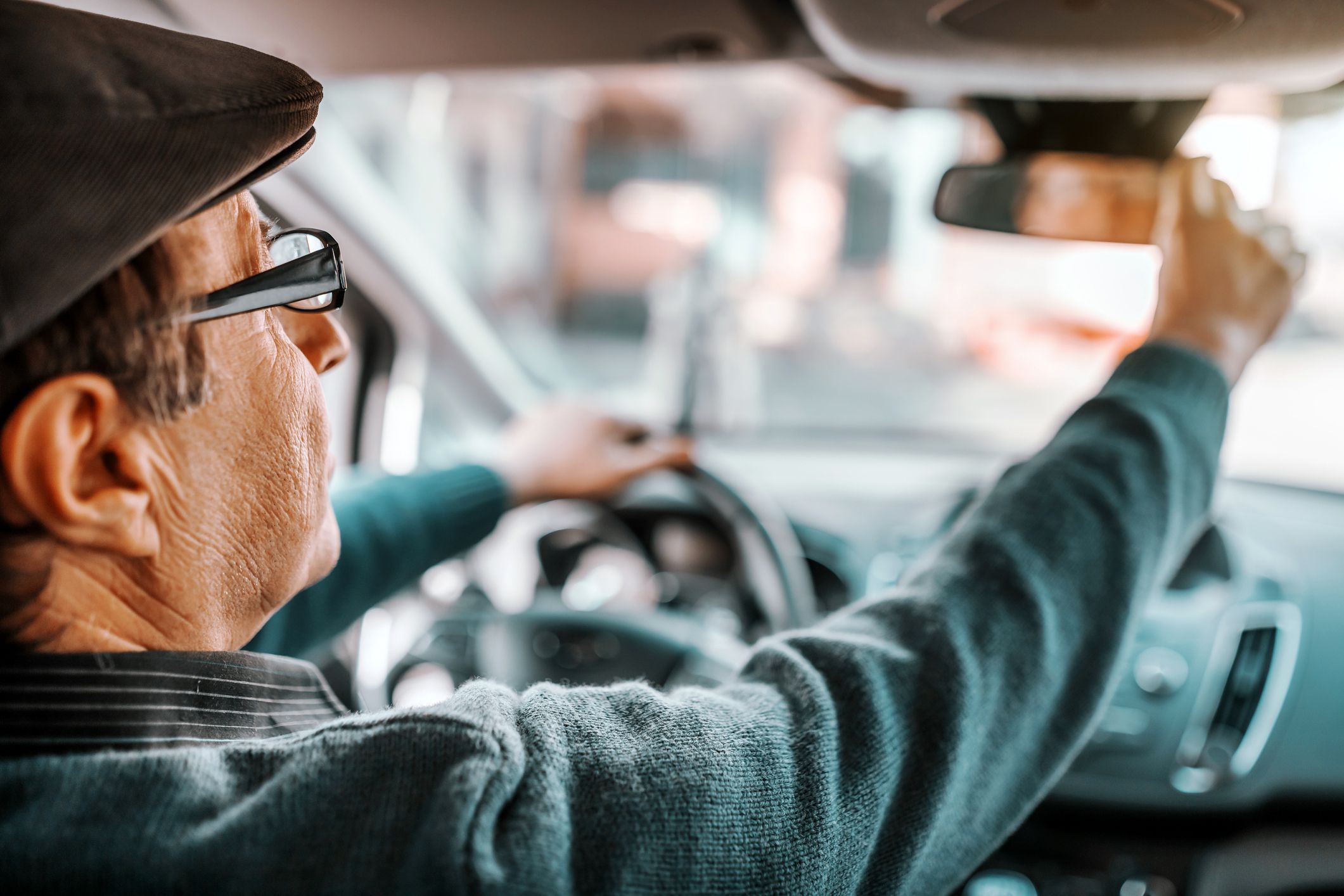 senior man driving, adjusting rearview mirror