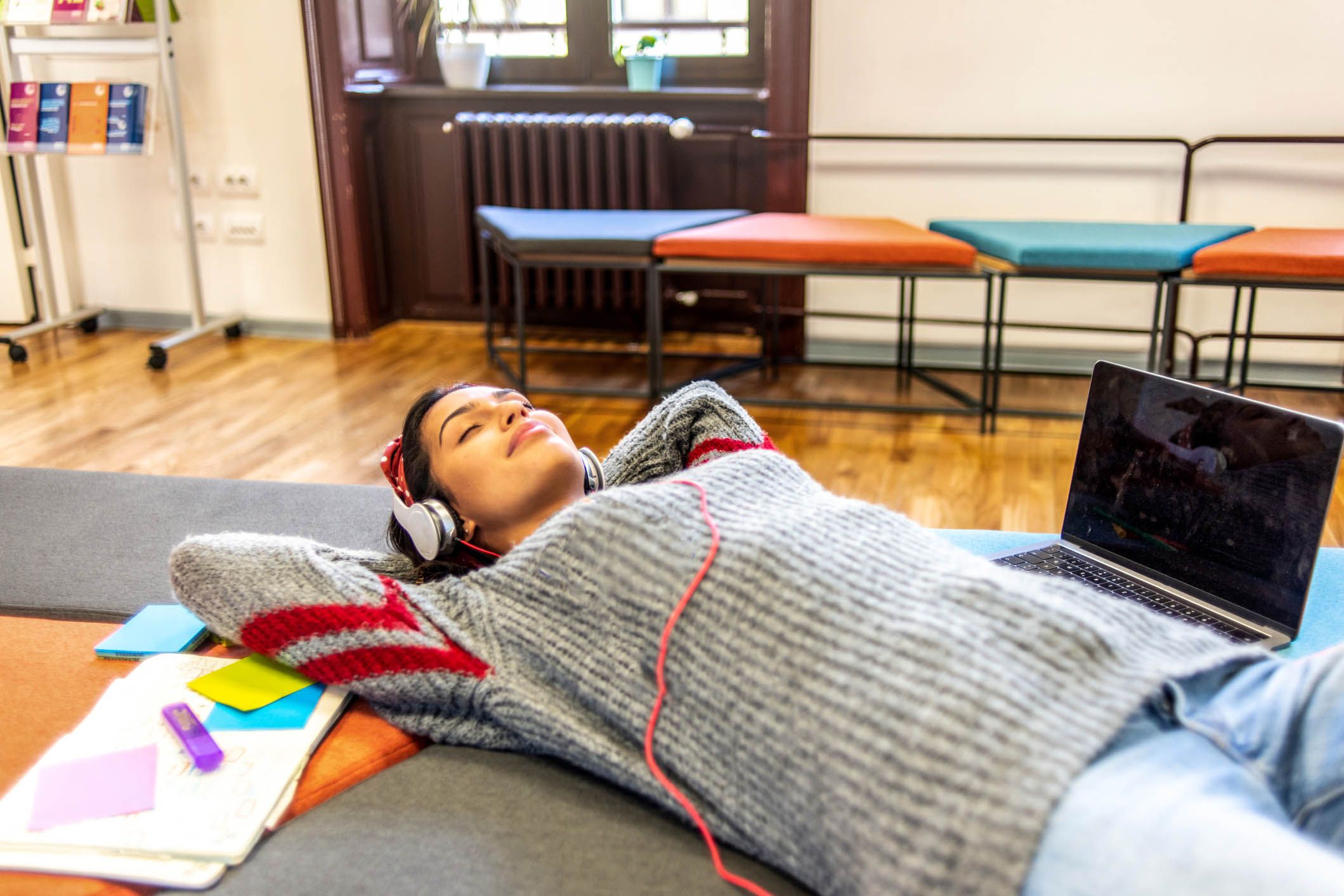 young woman laid back smiling and relaxing with eyes closed, with notebooks, highlighters, and laptops to her side