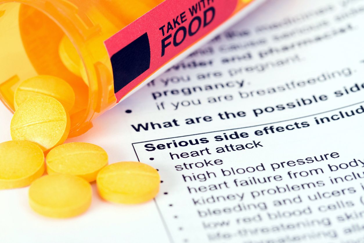 pills spilling out of bottle over paper listing serious side effects