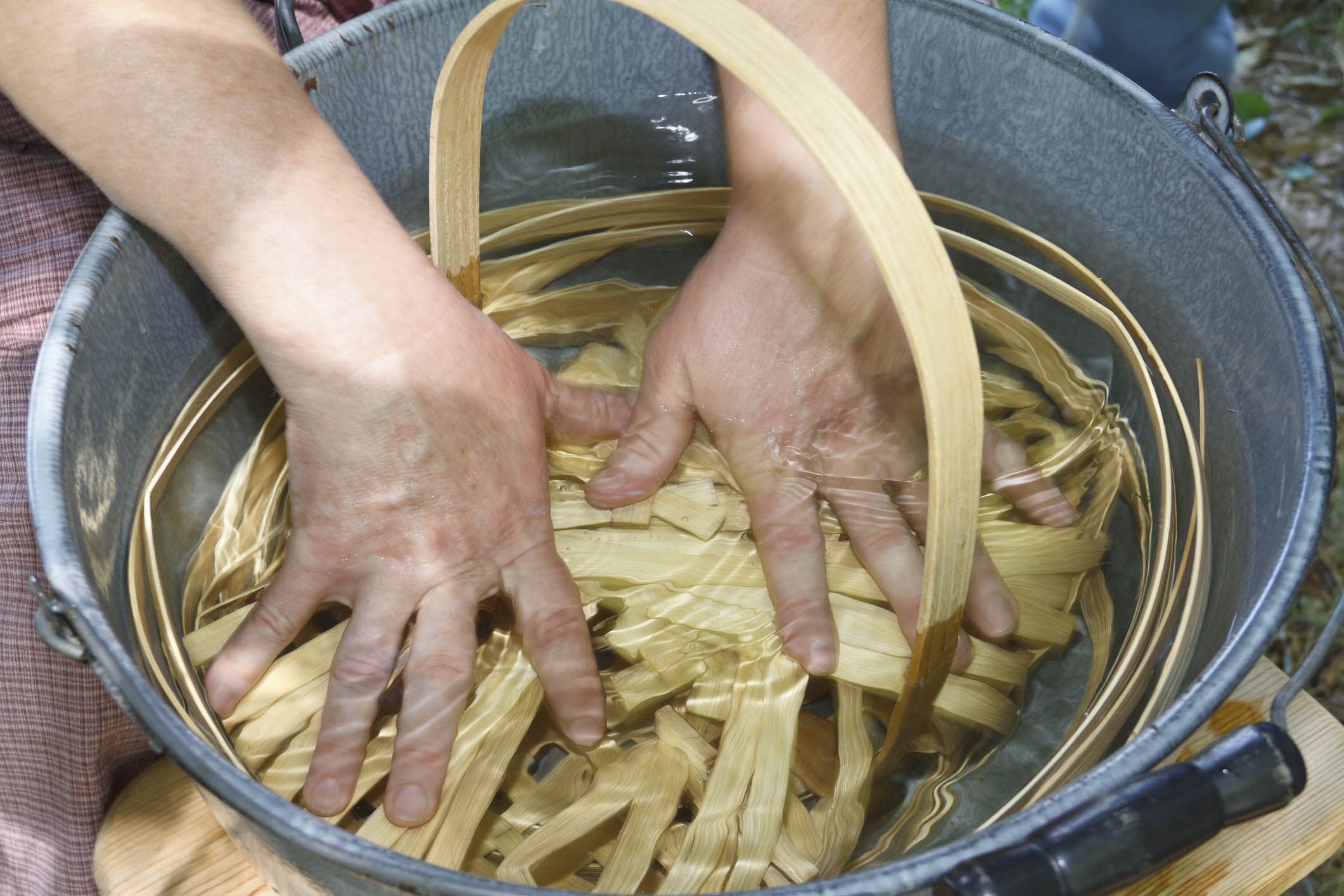 hands soaking basket material in bucket of water