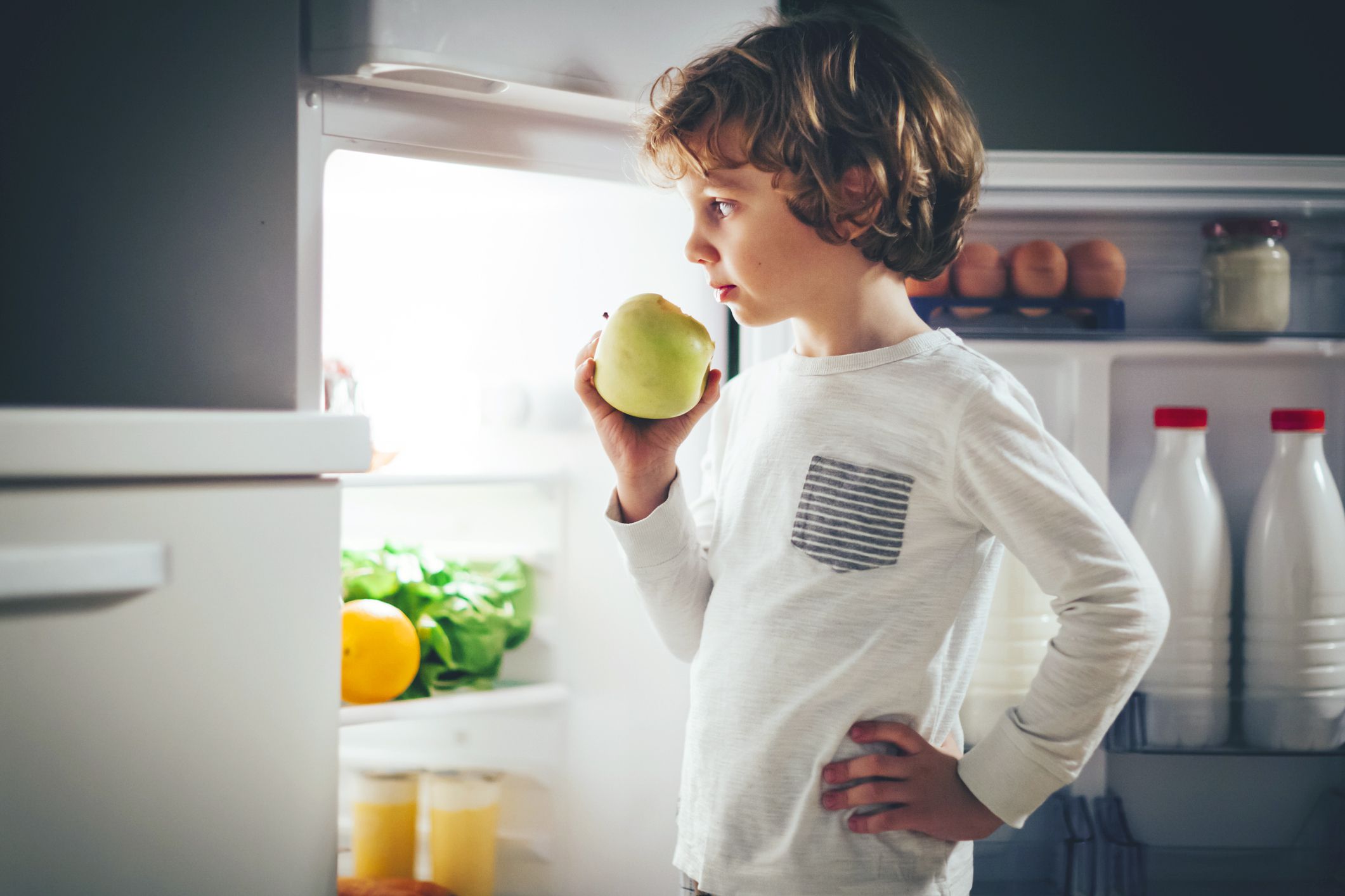 boy eating apple staring into fridge