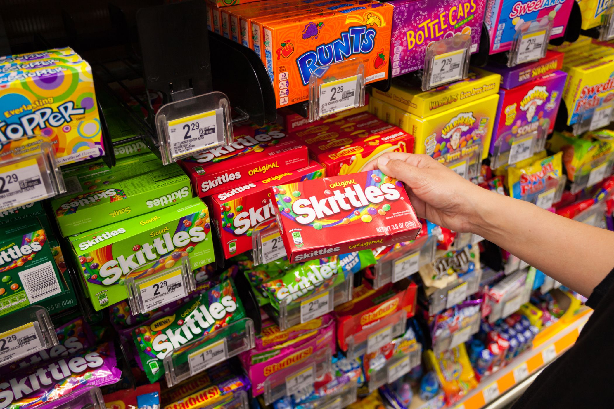 hand grabbing skittles from grocery store shelf