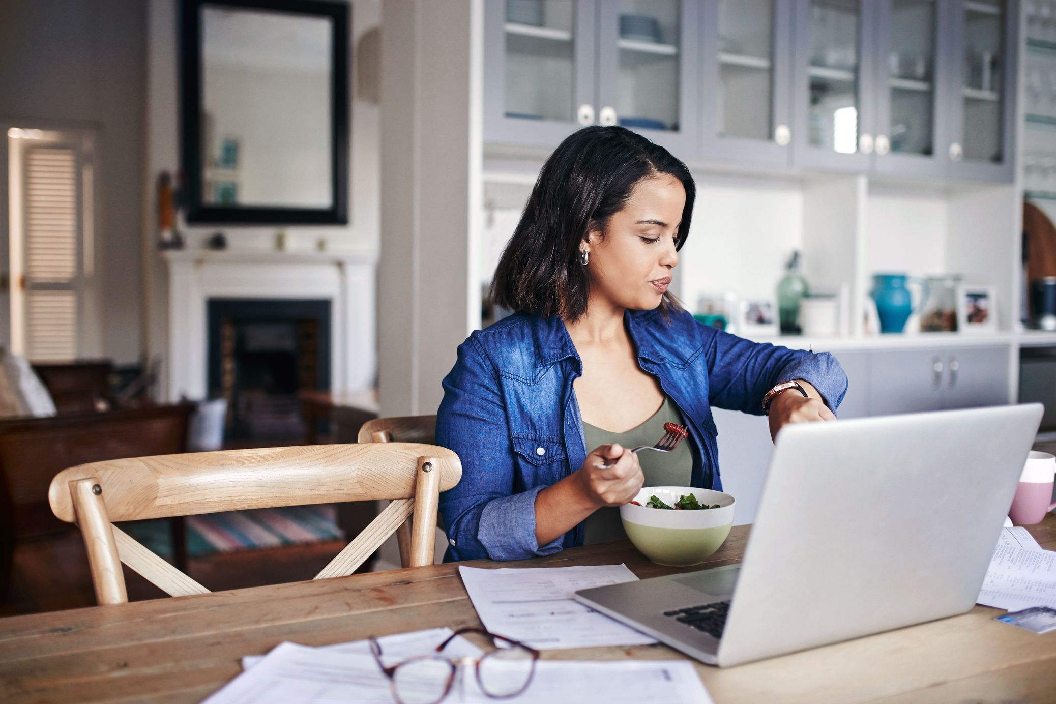 woman checking time sitting in kitchen with laptop on table