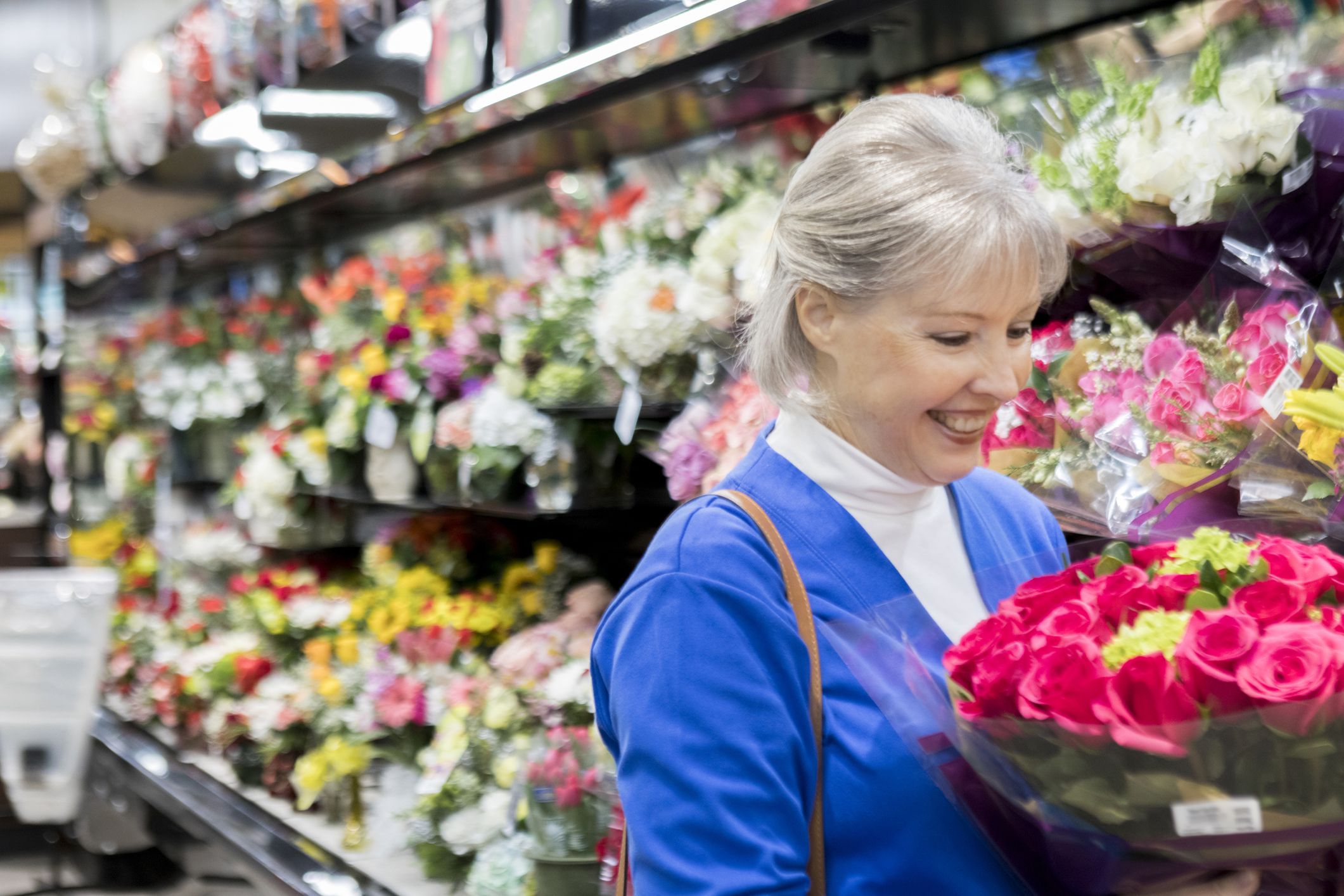 senior woman picking up flowers from grocery store