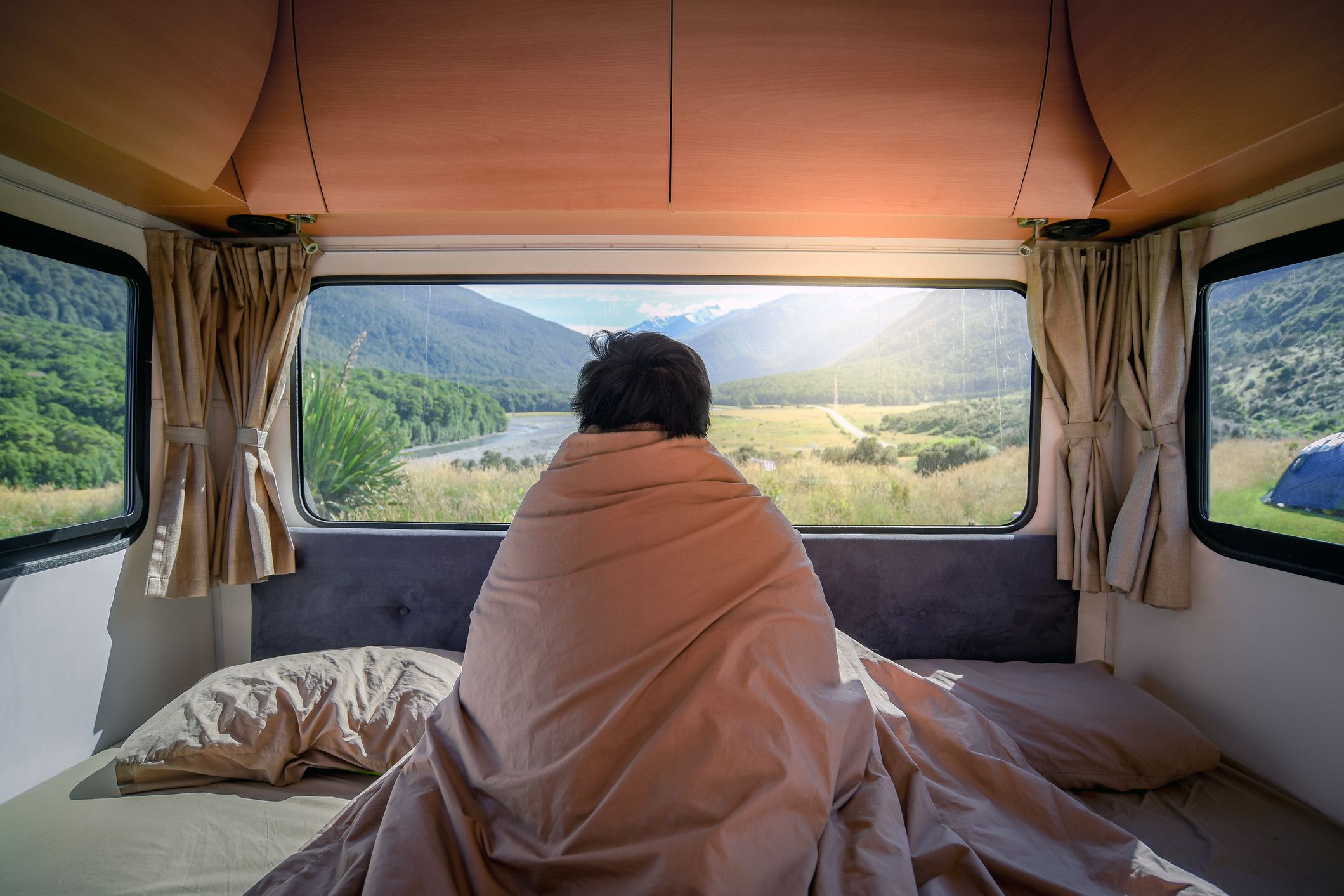 person's back staring out of rv into valley, wrapped in comforter