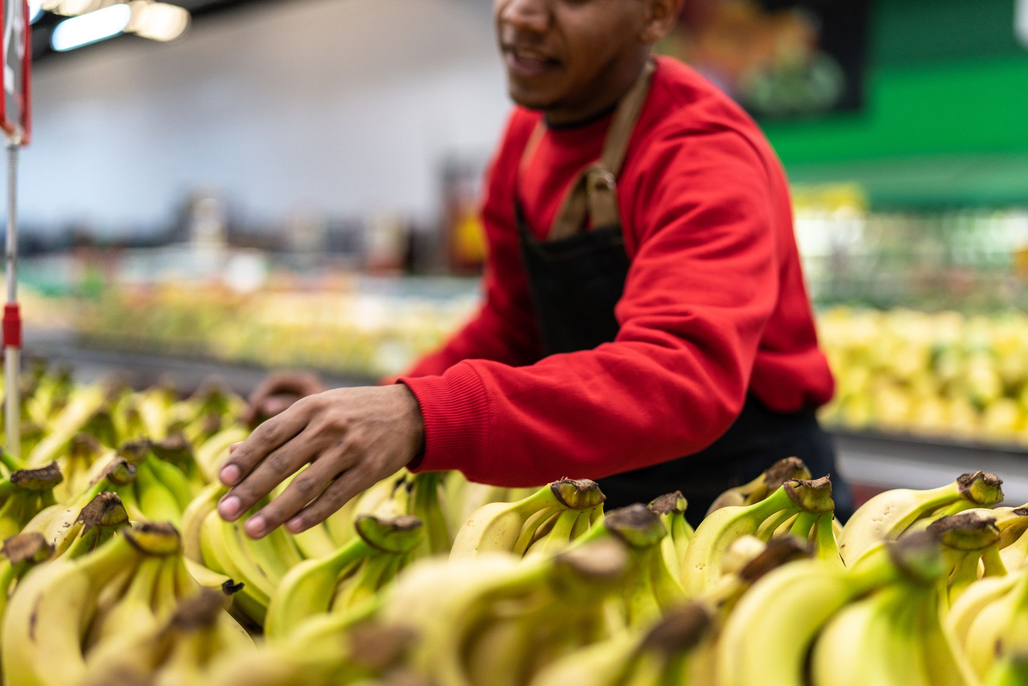 supermarket employee choosing less ripe bananas from produce area
