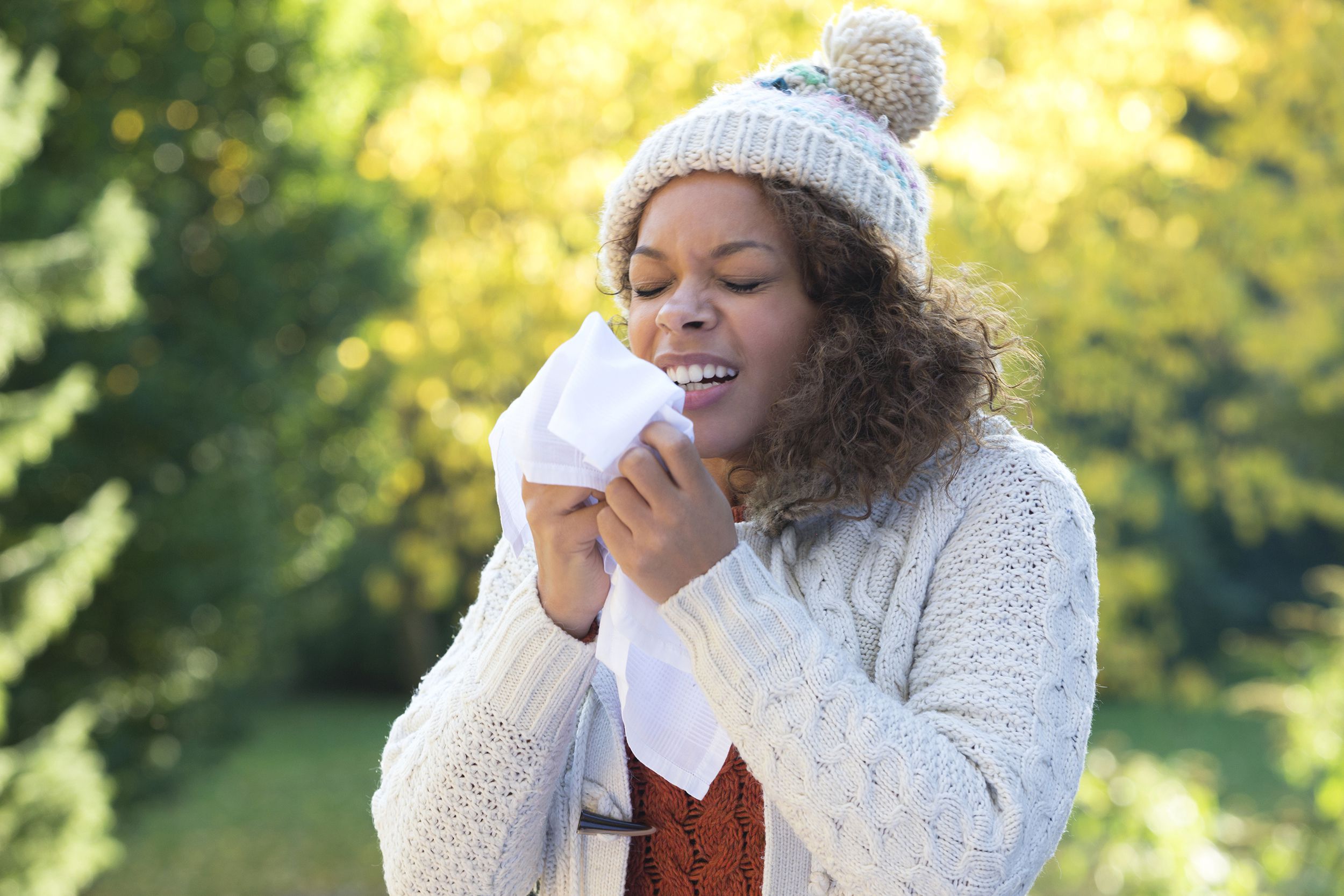 woman outside during early fall, sneezing