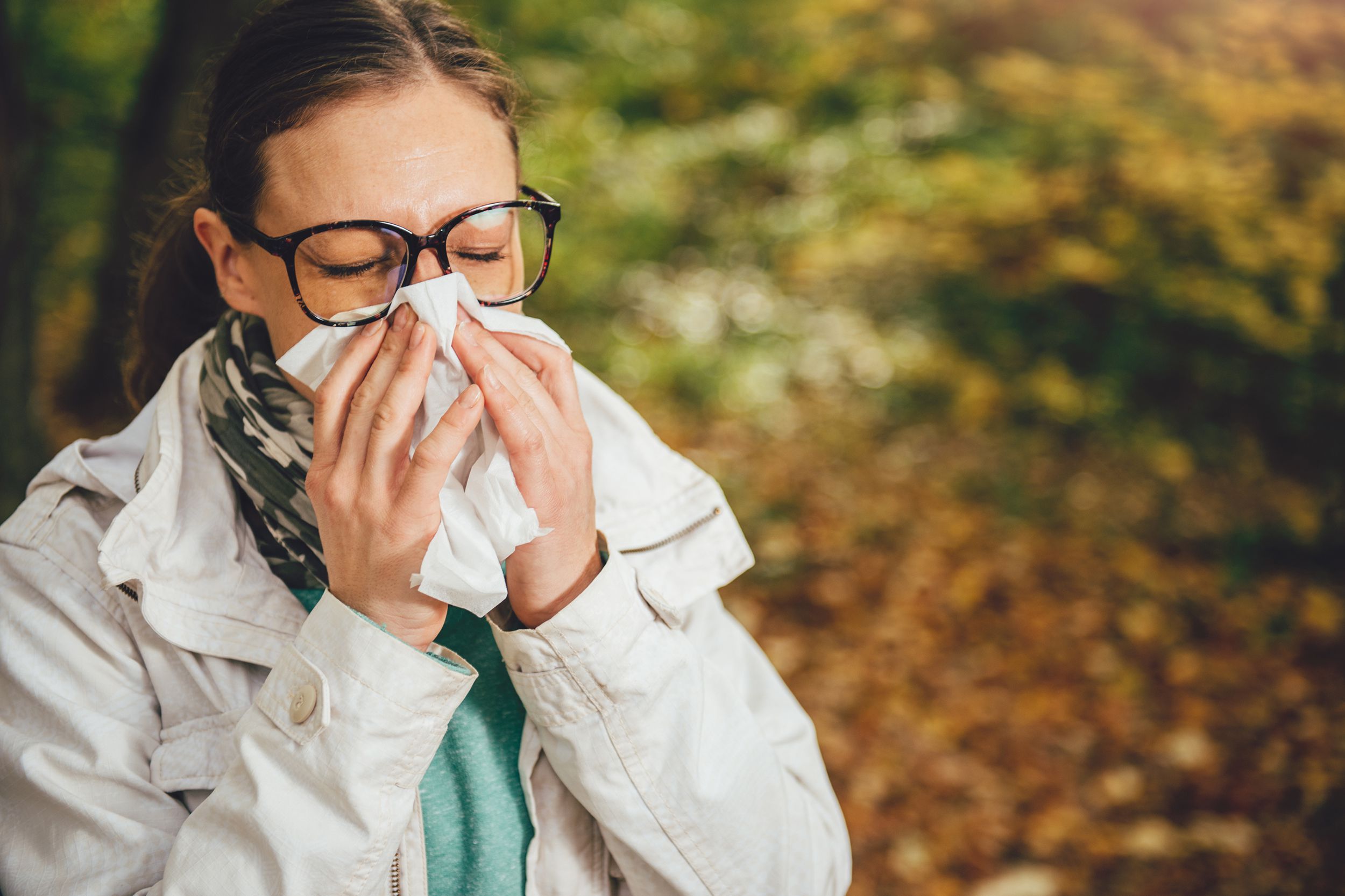 woman blowing her nose outside during fall