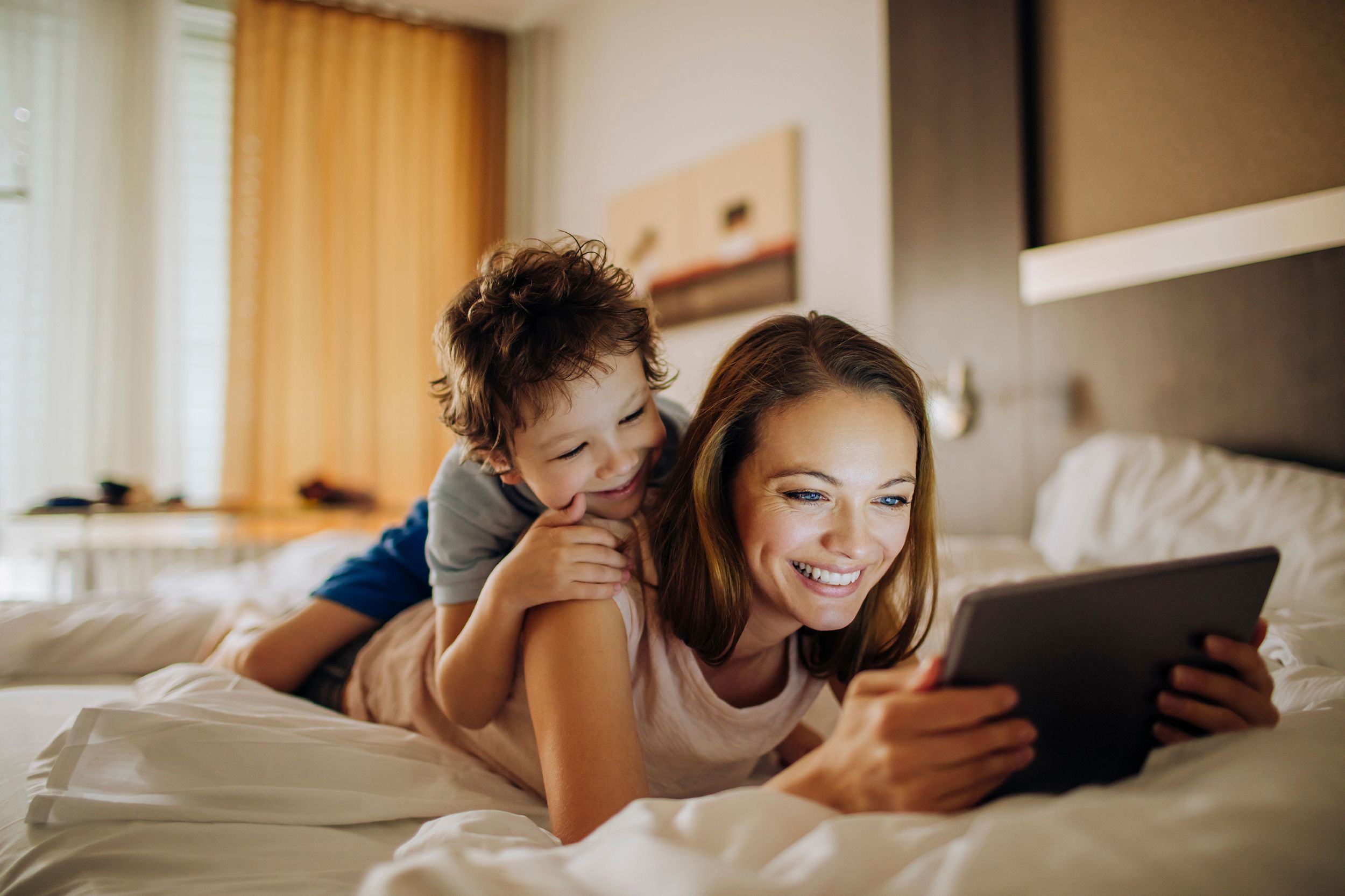mother and son laying on bed using a digital tablet in hotel room