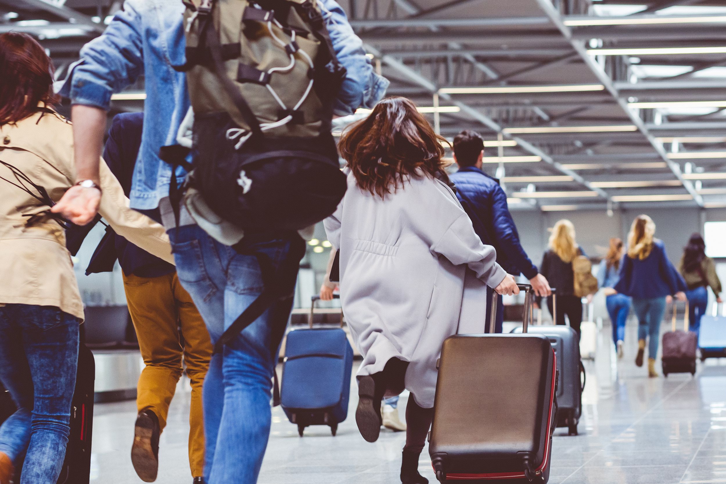 passengers jogging with luggage in airport corridor