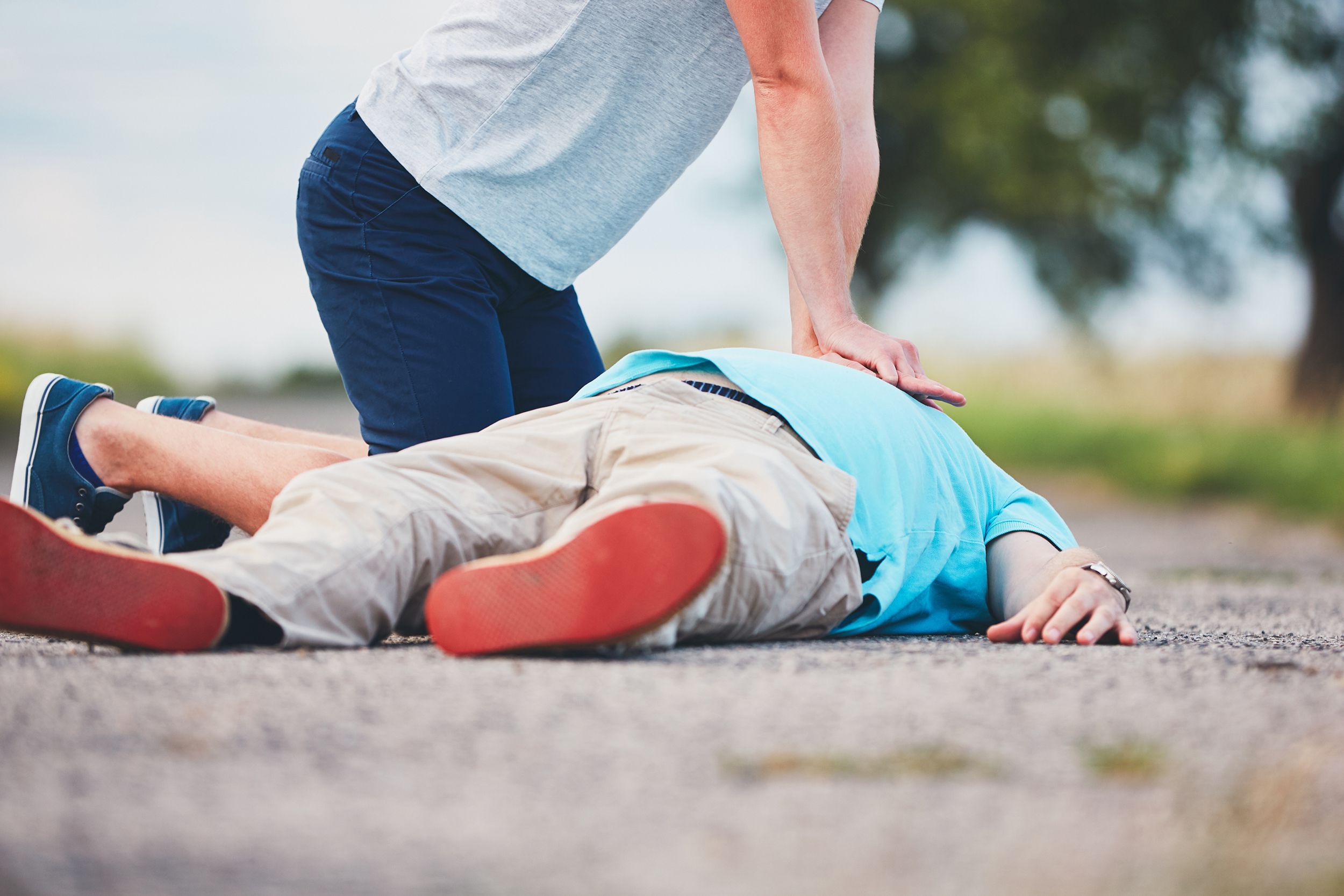 senior man receiving CPR on a rural road by another man
