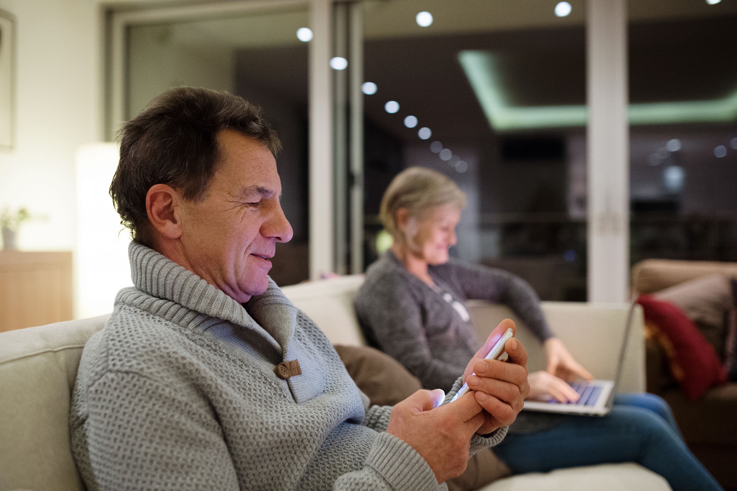senior couple with laptop and smartphone sitting on couch