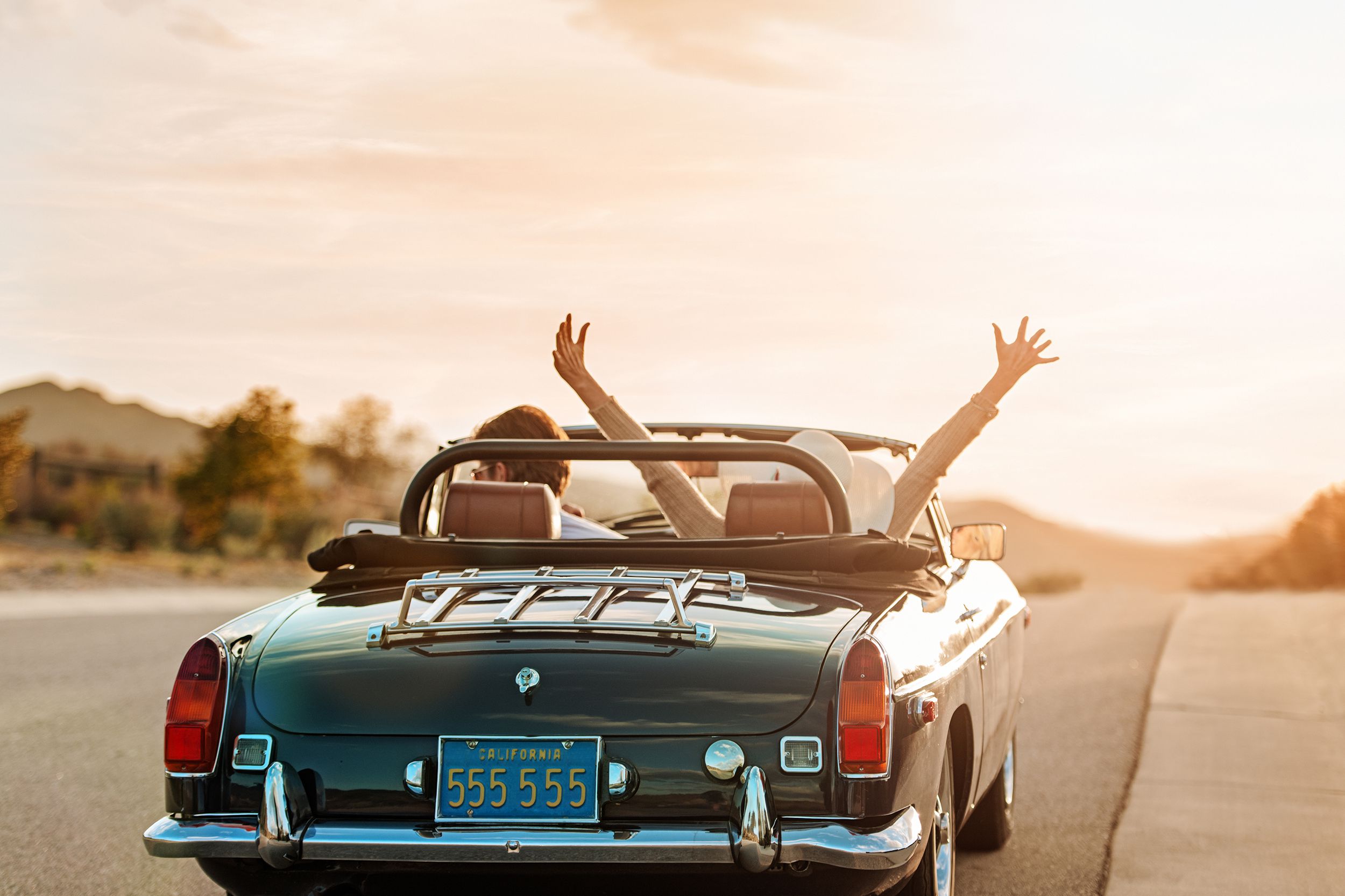middle-aged couple in convertible car driving while the sun is setting