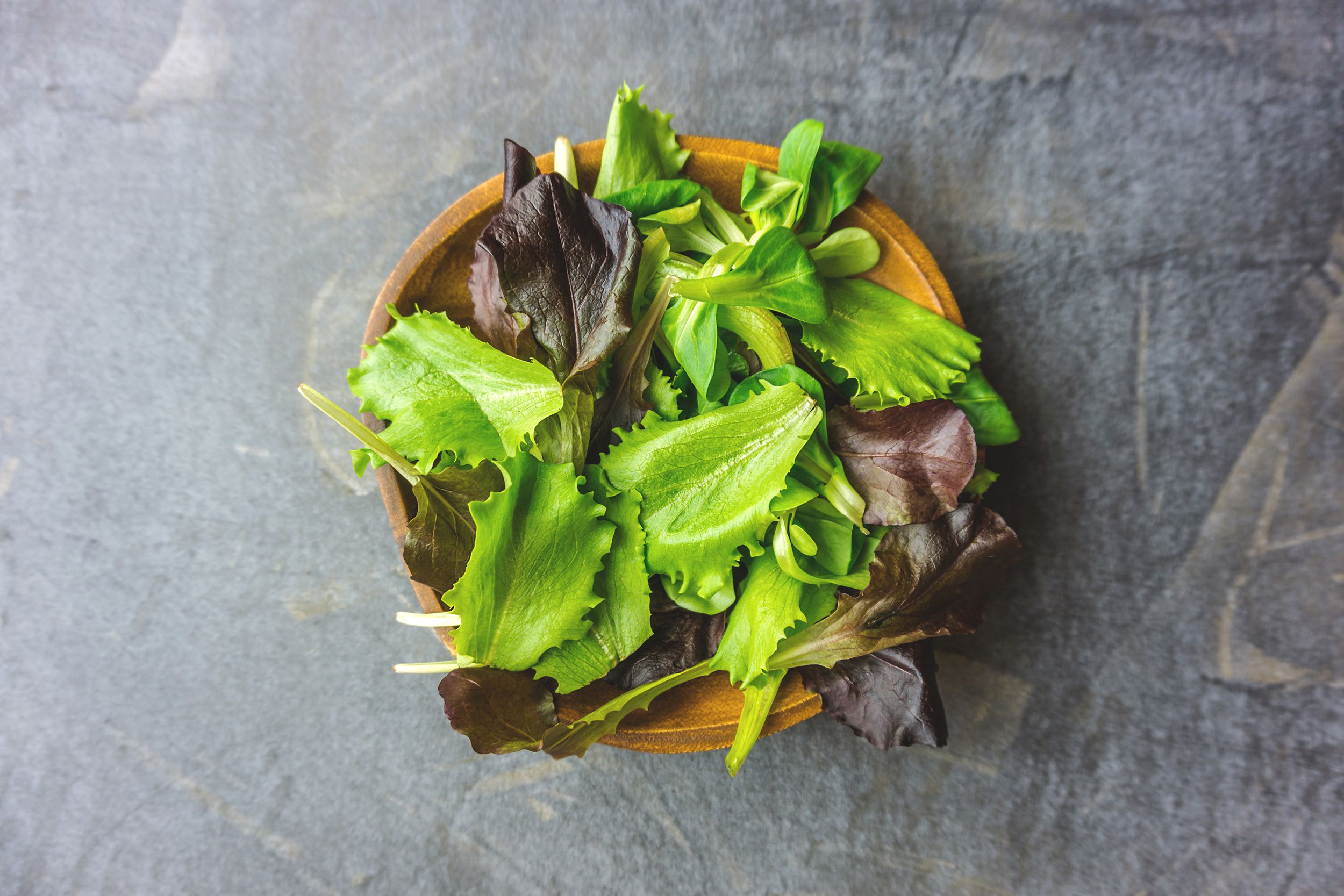fresh green leafy salad in wooden cup on dark stone background