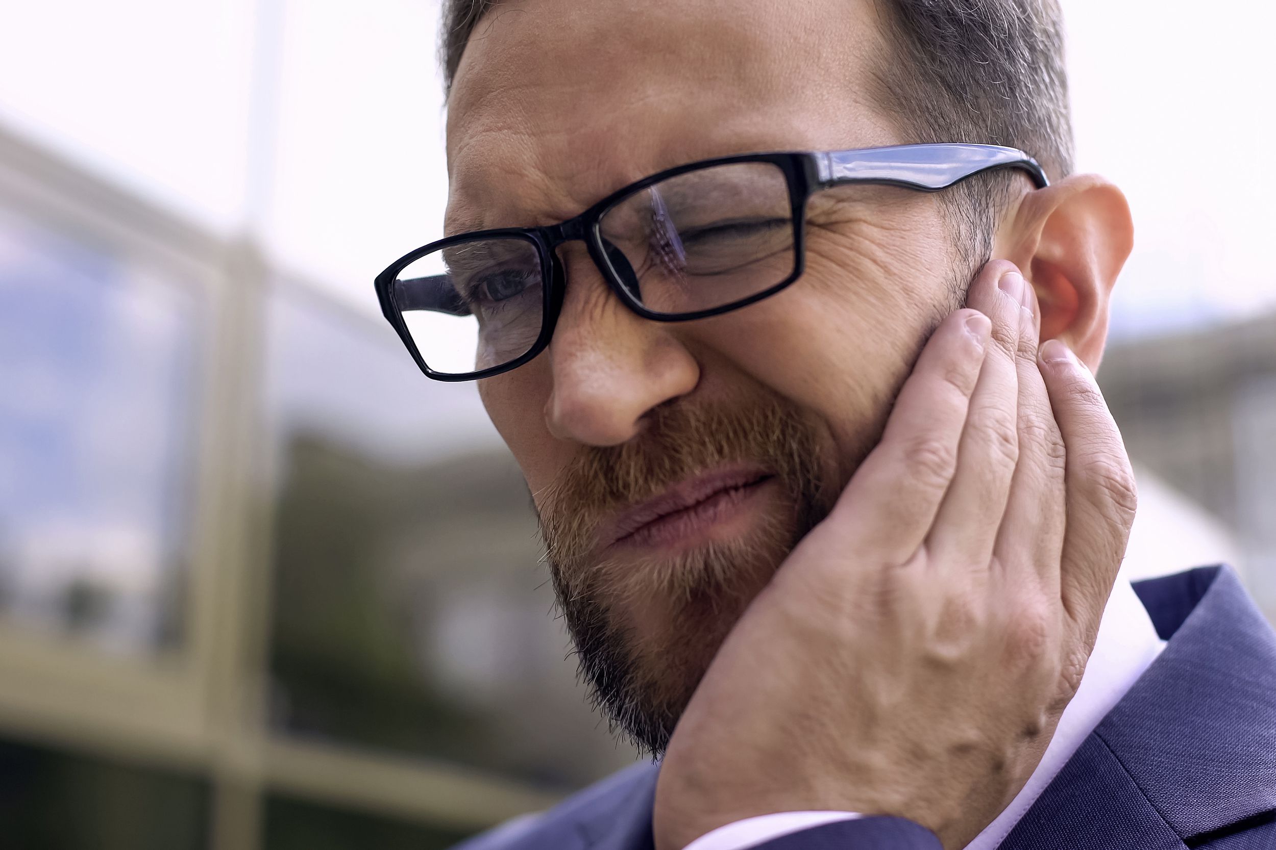 man with eyeglasses has ear pain while walking outside