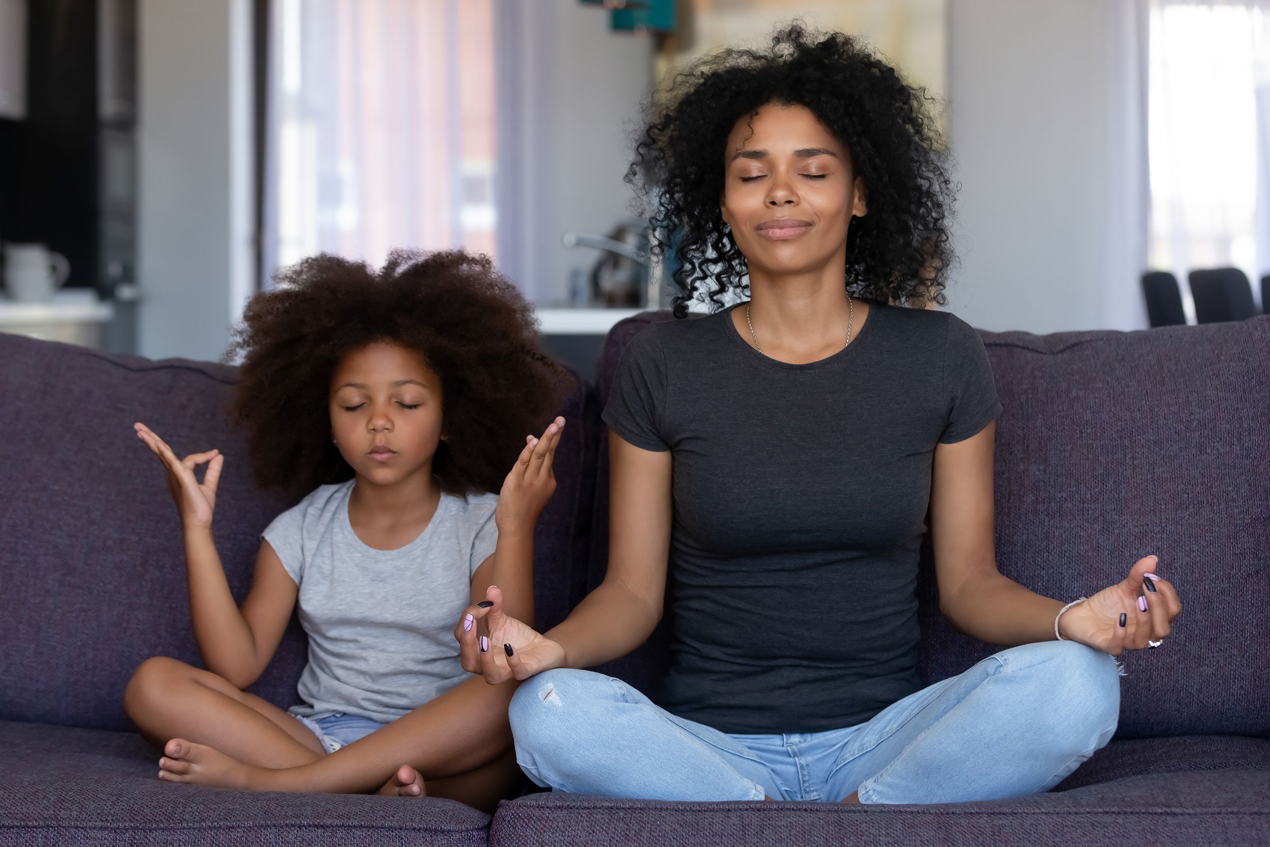 mom with funny kid daughter meditating on couch together