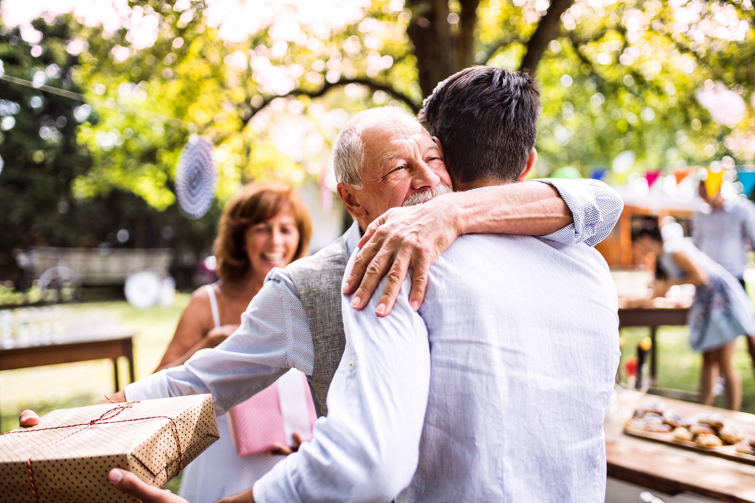 family celebration outside with grandfather giving grandson a gift and hug
