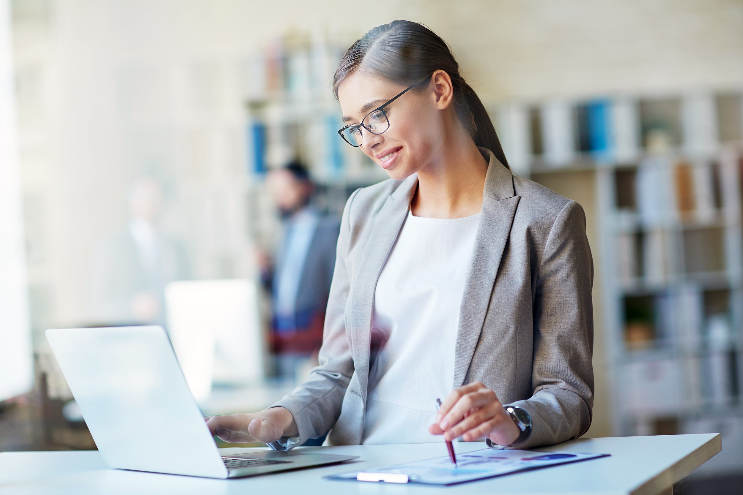 young intelligent woman standing in office space at her desk with laptop