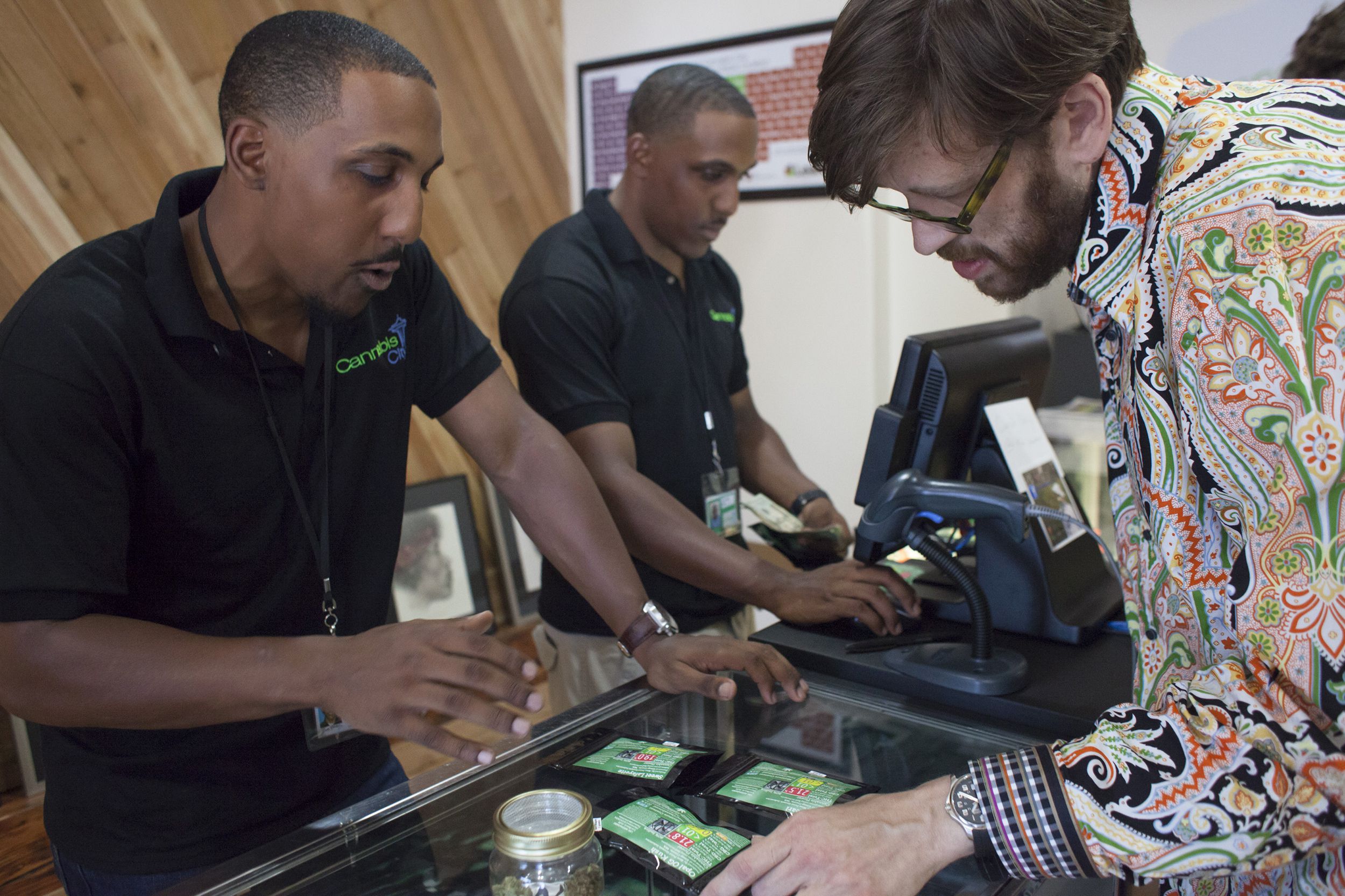 Identical twins Adam Powers (L) and Andrew Powers (C) serve customer Michael Merithew (R) at the Cannabis City retail marijuana store on July 8, 2014 in Seattle, Washington.