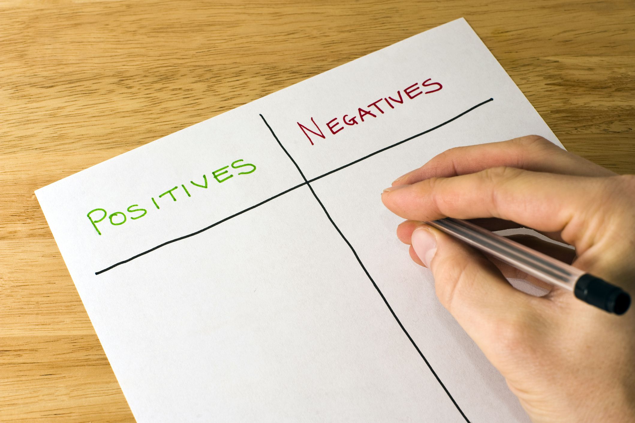 hand holding pen about to start filling in list of positives and negatives