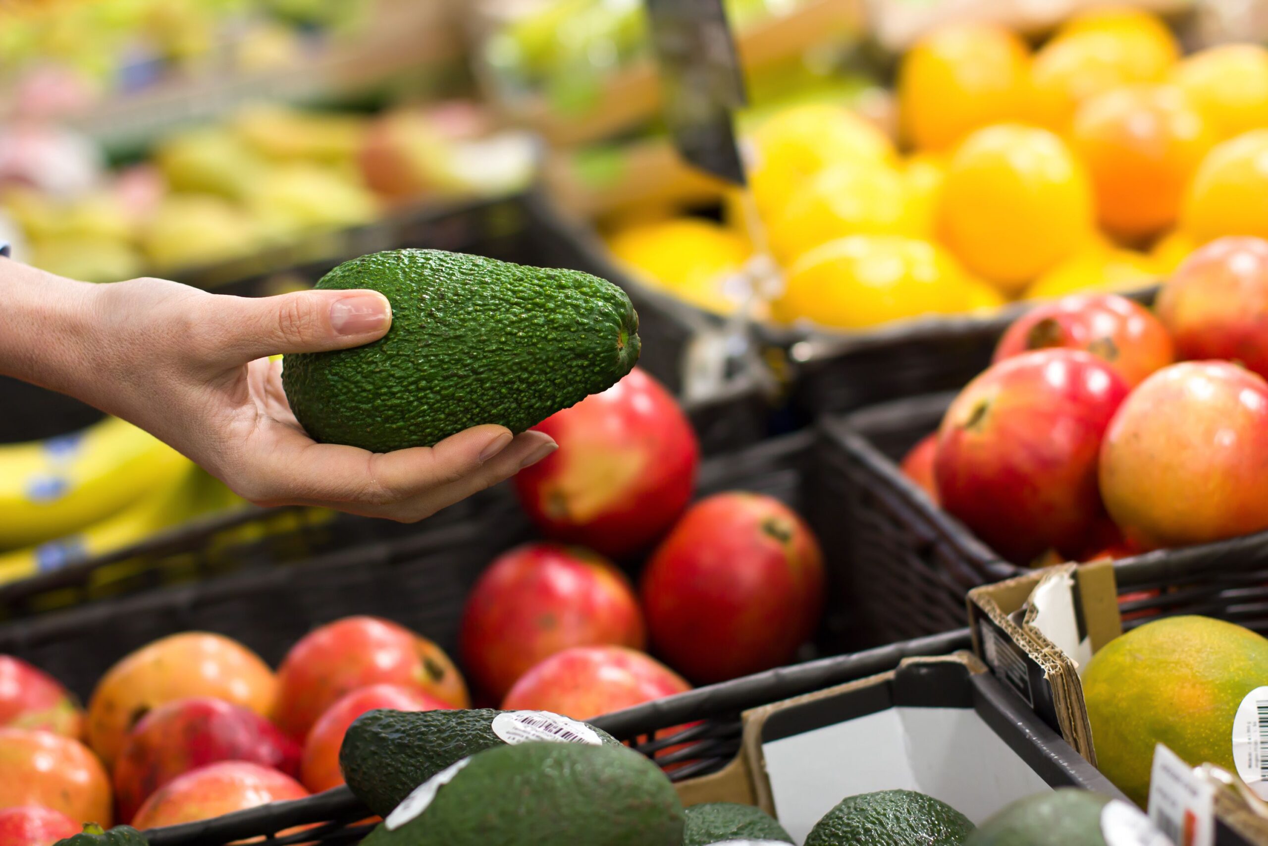 hand picking up avocado at grocery store