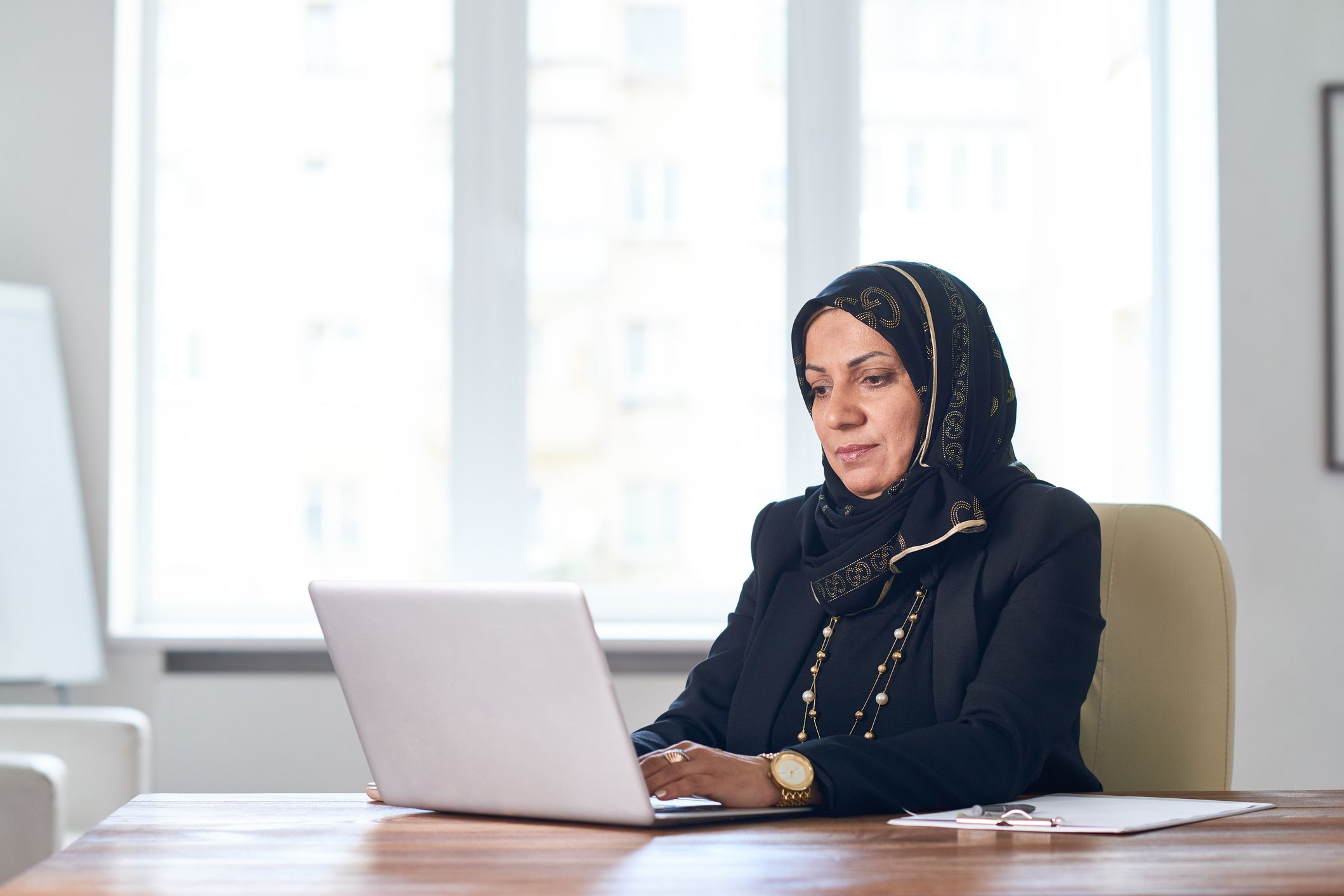 woman using laptop in office, clipboard to her side