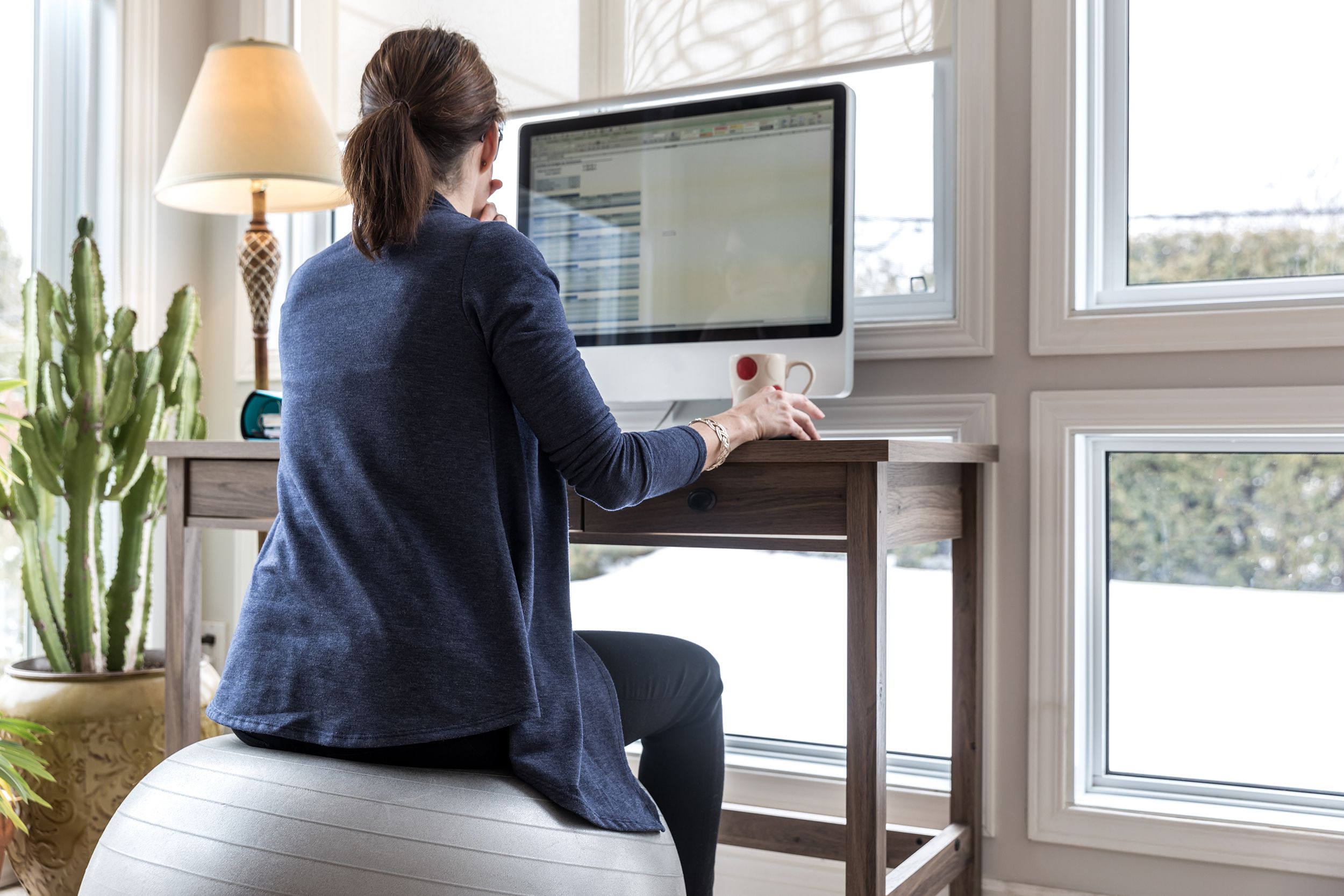 woman working from home at desk with computer, sitting on exercise ball
