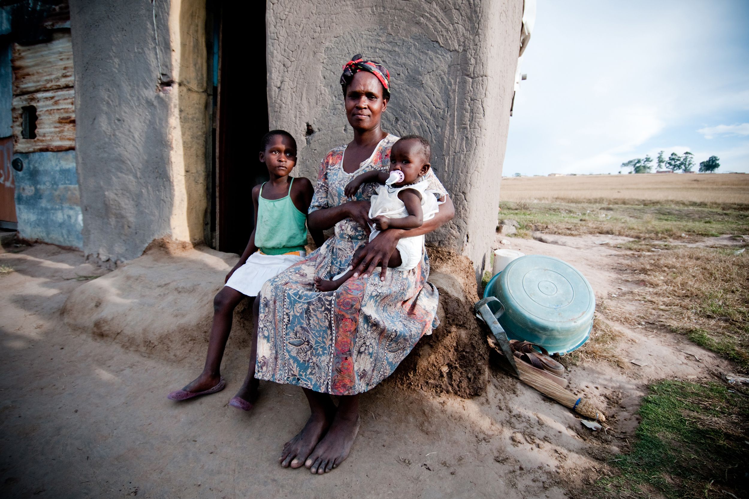 poor African family sitting in front of a shanty hut