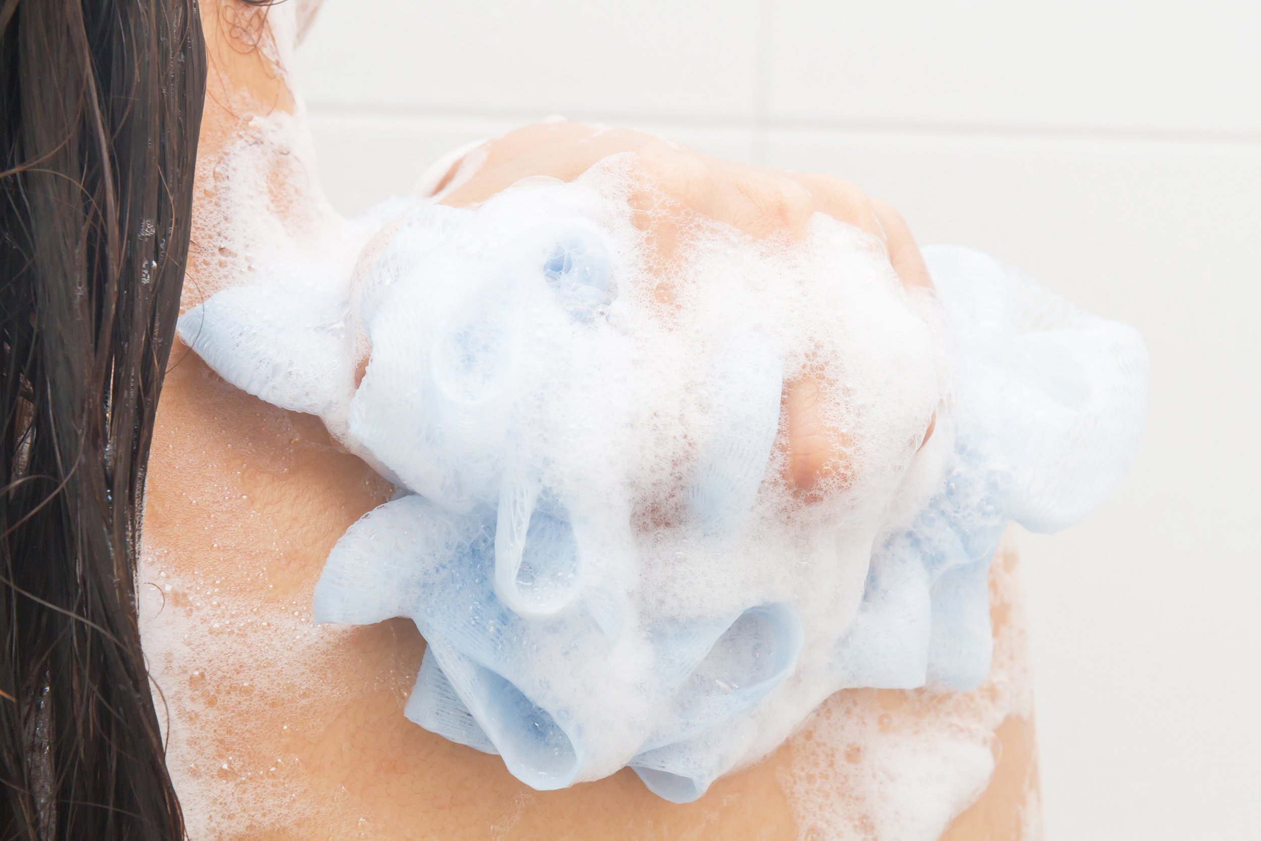 woman take a shower and clean her back with puff
