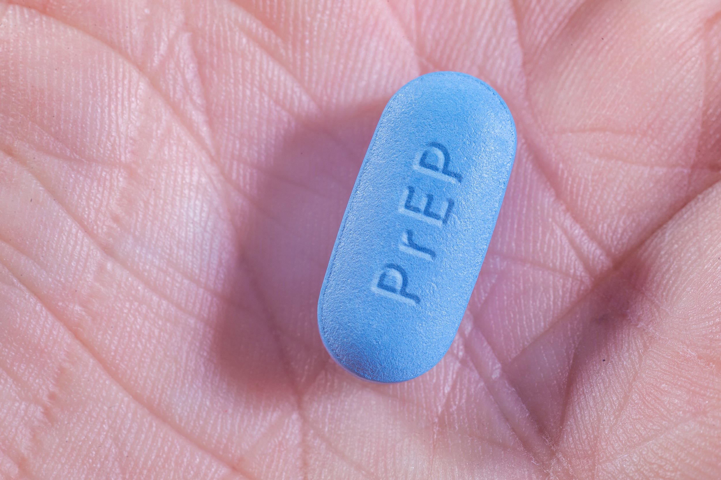 A close-up of a single blue pill labeled "PrEP" resting on the palm of a person's hand.