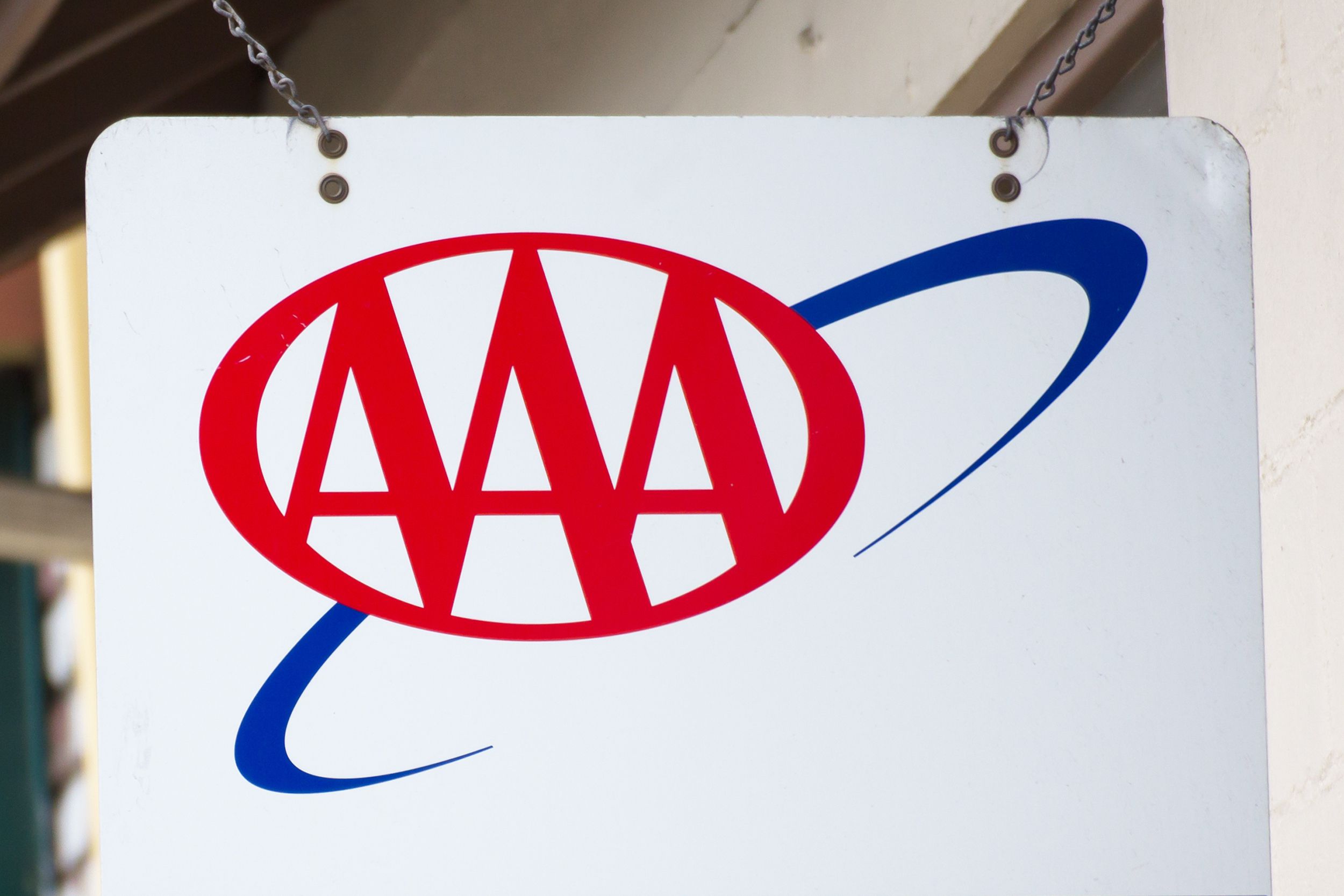 AAA logo on left side of a hanging blank white sign, blurred background along sides of outside of building