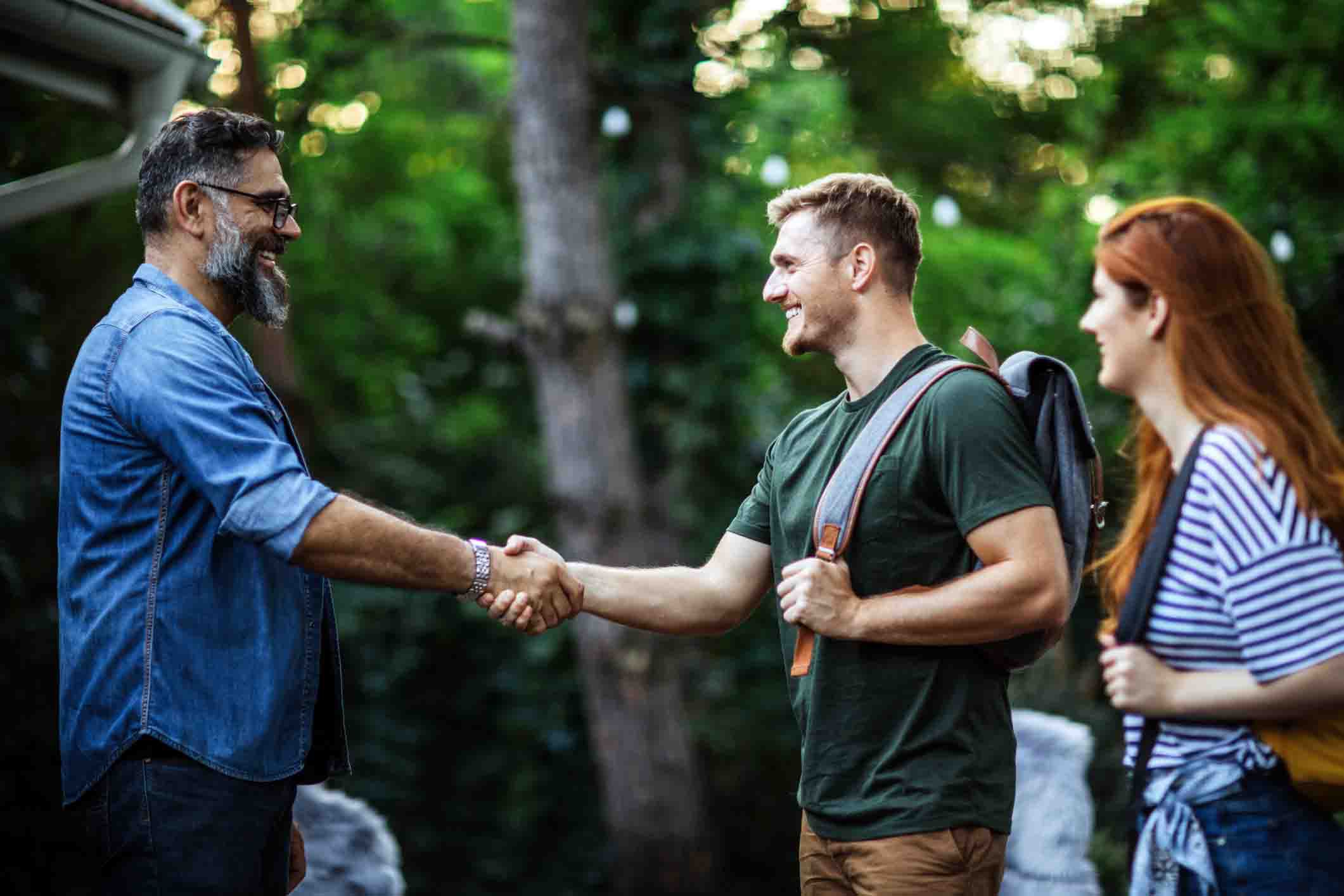 host welcoming guests with backpacks outside house