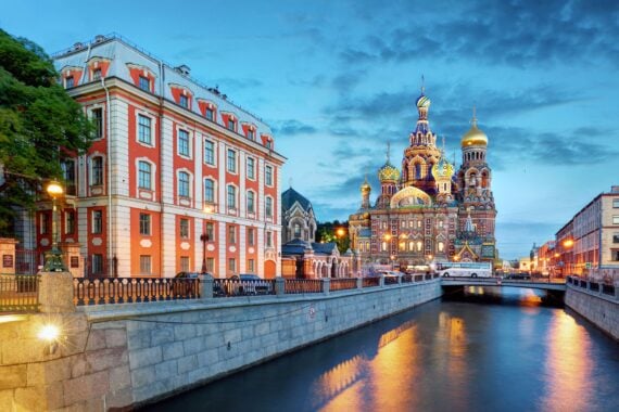 A canal runs past colorful historic buildings and the ornate Church of the Savior on Spilled Blood in St. Petersburg, Russia, at dusk.