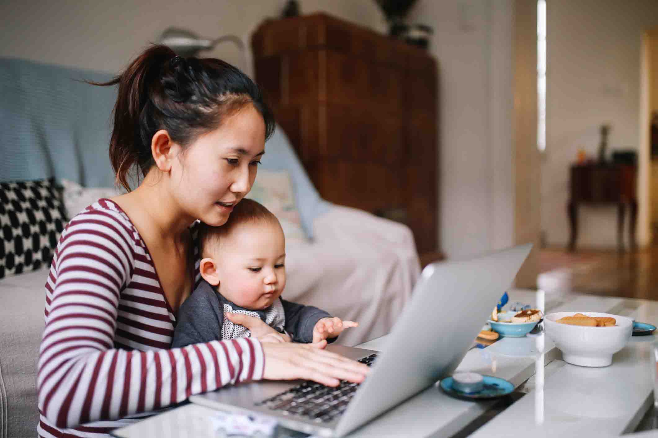 mother holding child while navigating website on laptop