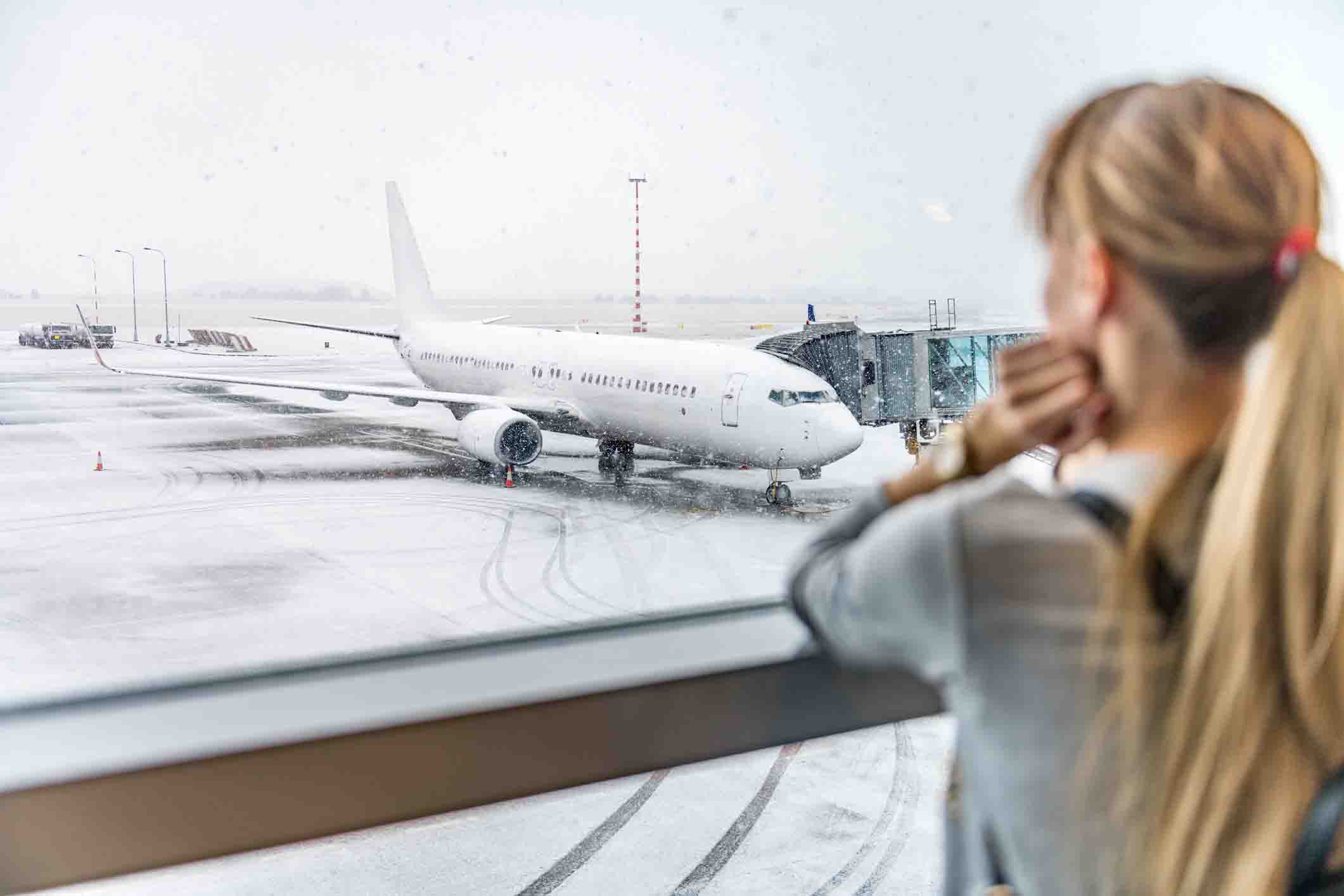 young woman at airport looking out window at plane