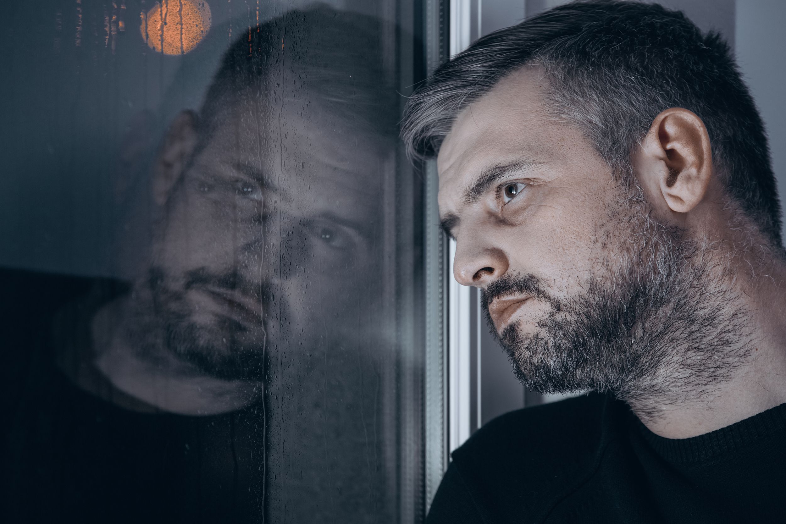 sad man with depression looking out of window