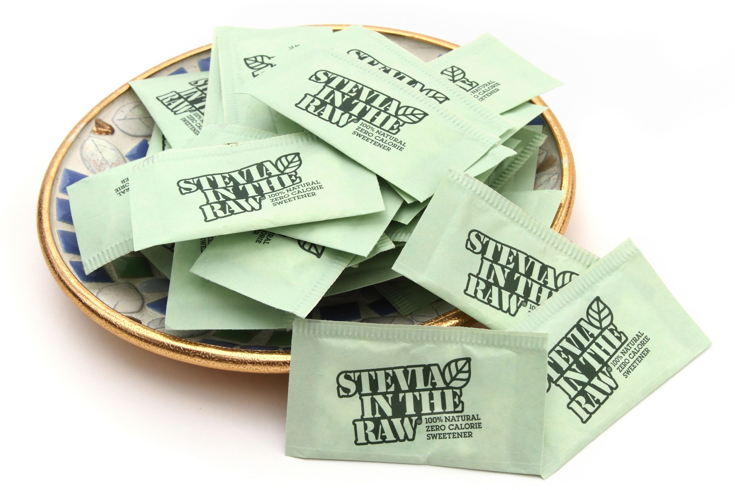 Individual packets of Stevia in the Raw, a zero calorie natural sweetener, are loosely piled on a saucer.