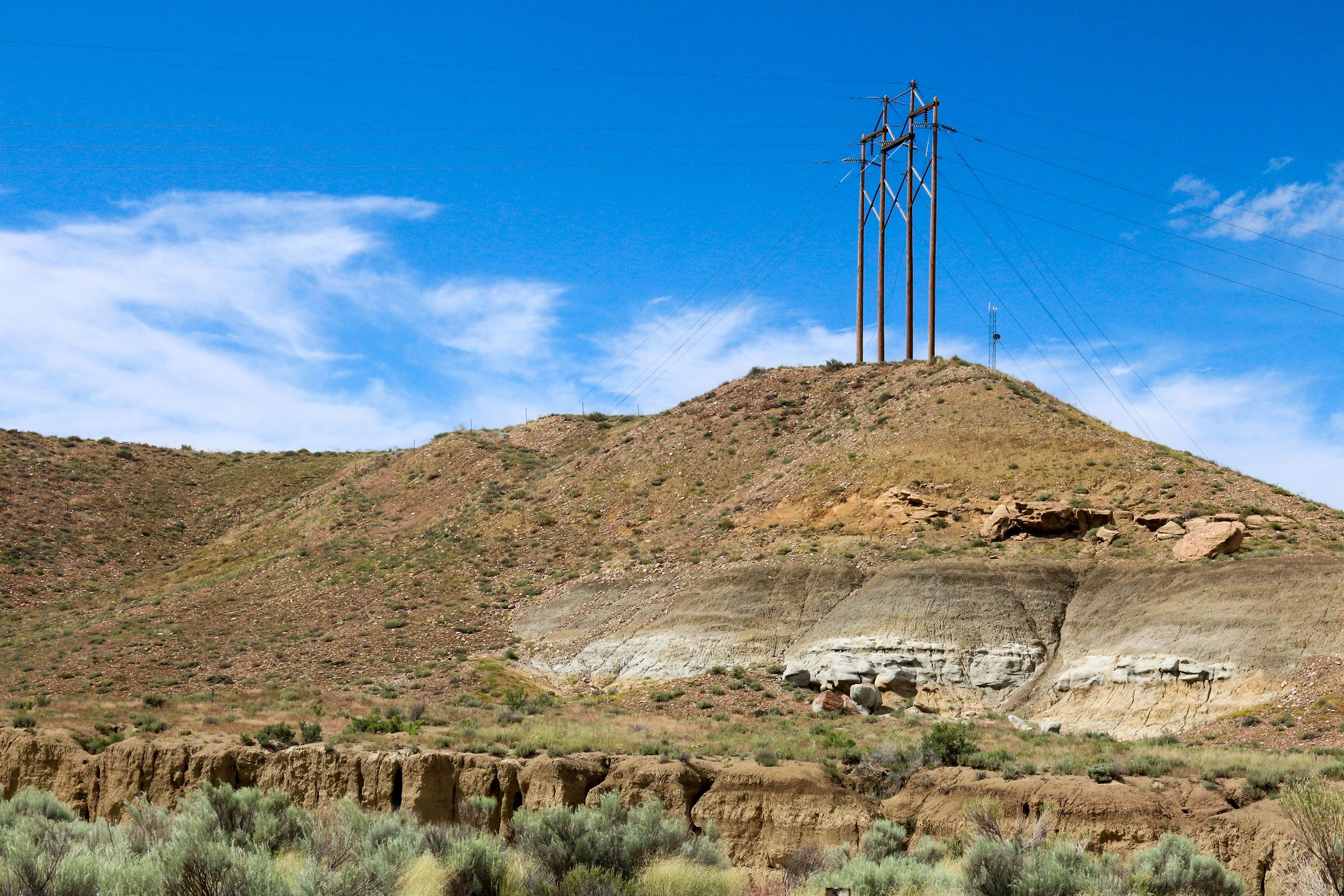 large power line installed on top of a light brown barren hill, New Mexico