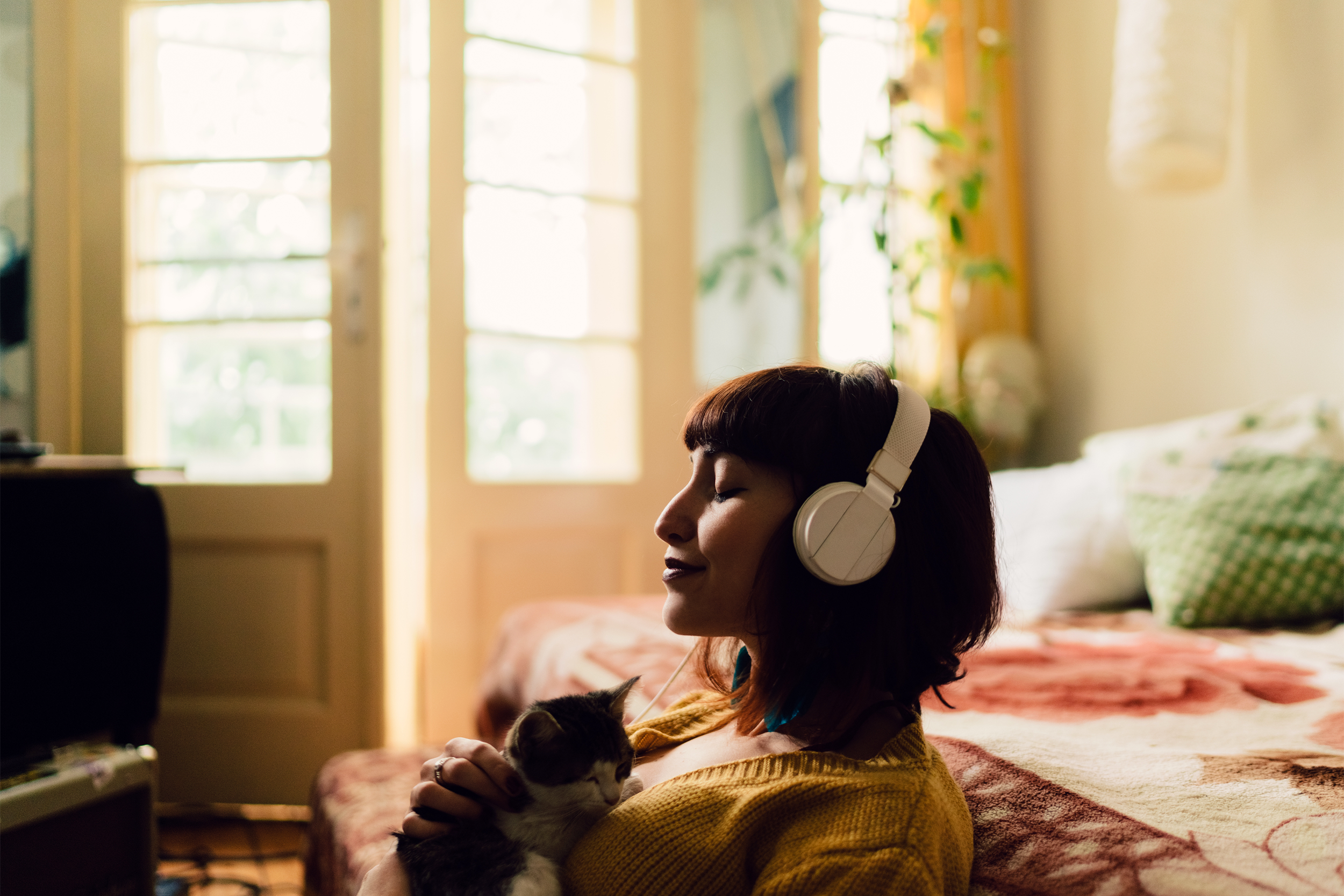 Young woman sitting in room listening to music with cat