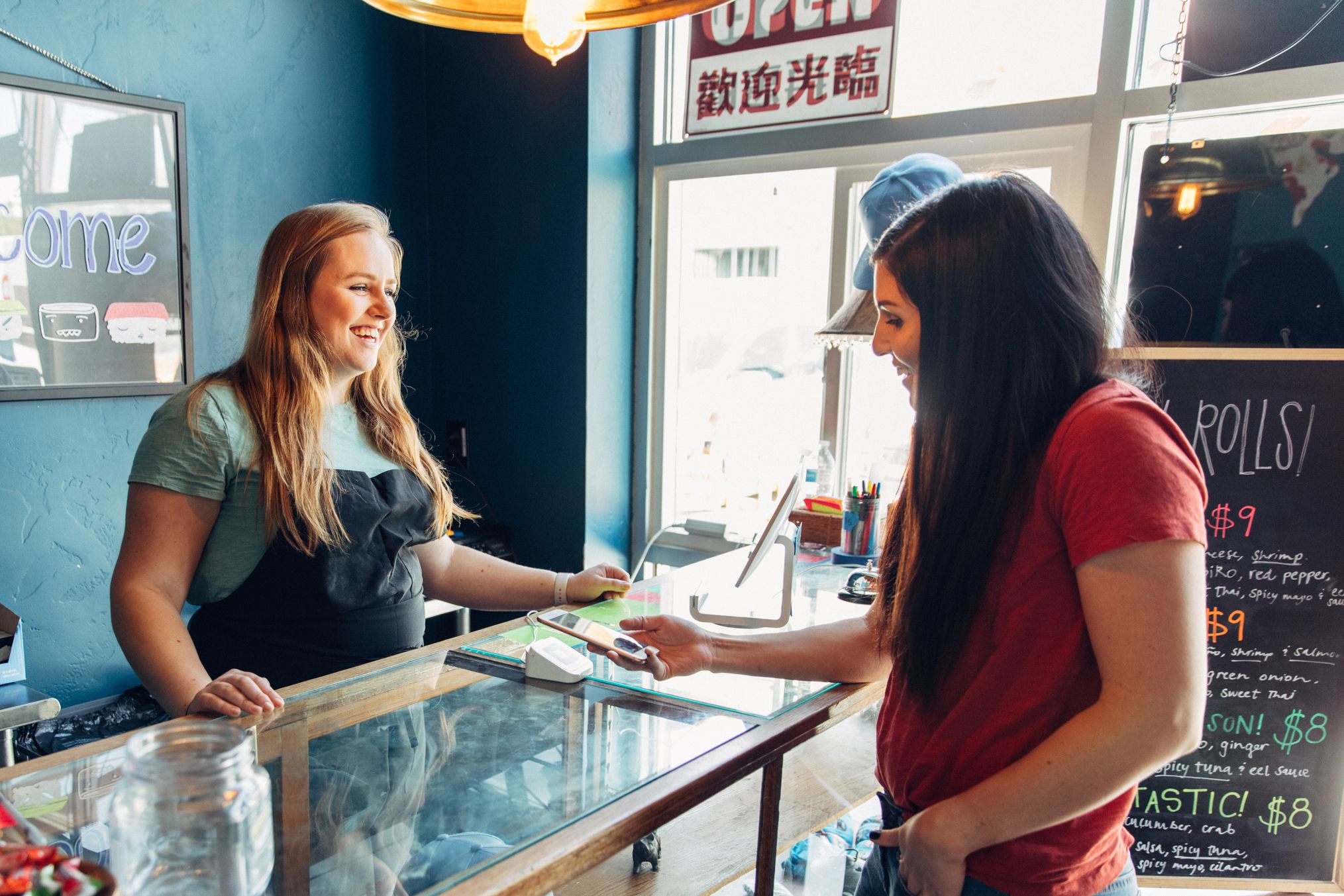 a woman of the millennial generation is using contactless payment to pay for lunch at a local sushi restaurant