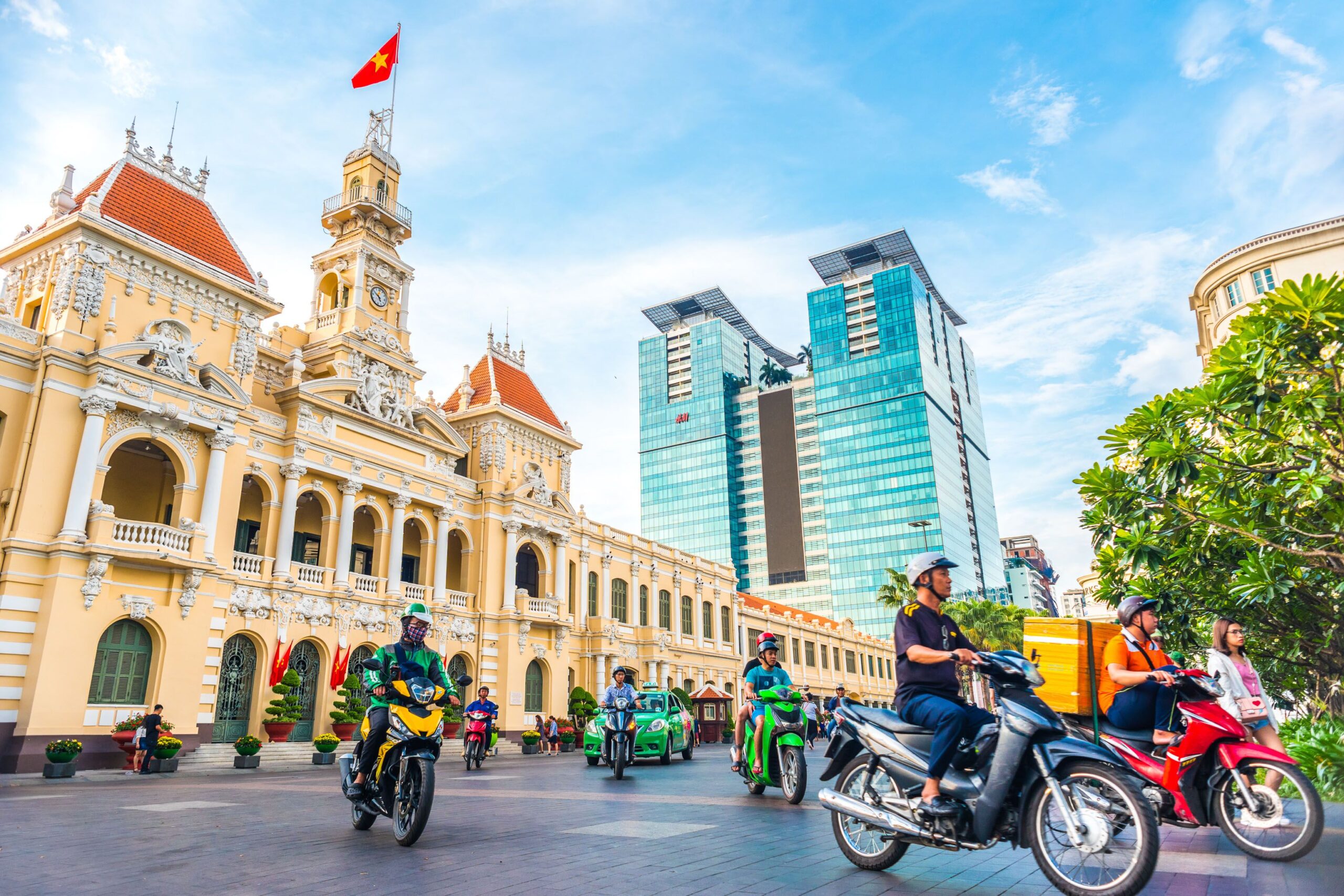 saigon city hall, vincom center towers, colorful street traffic (people driving motorbikes) & tropical plants against the blue sky