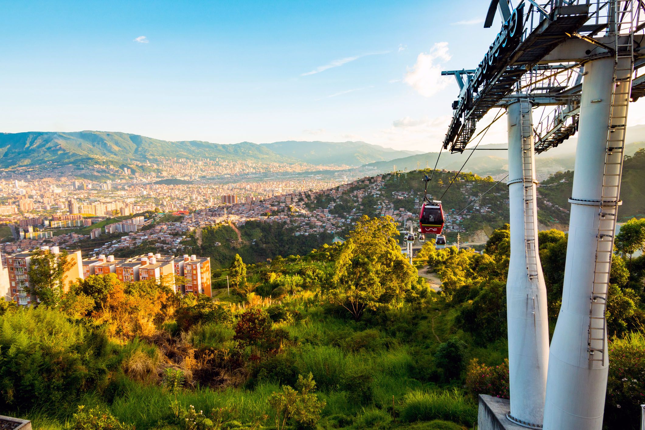 cars going up the metro cable system in medellin, colombia and the mountainous view of the andes and the city buildings during the afternoon seen in the background