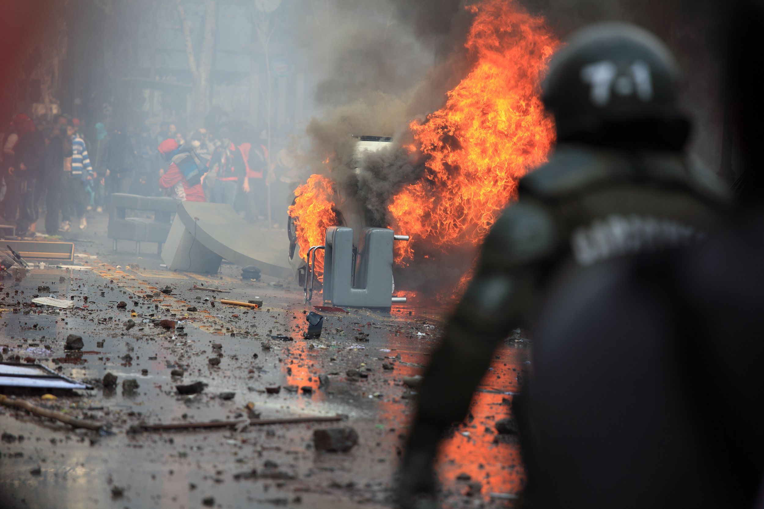 car on fire with protestors in the street