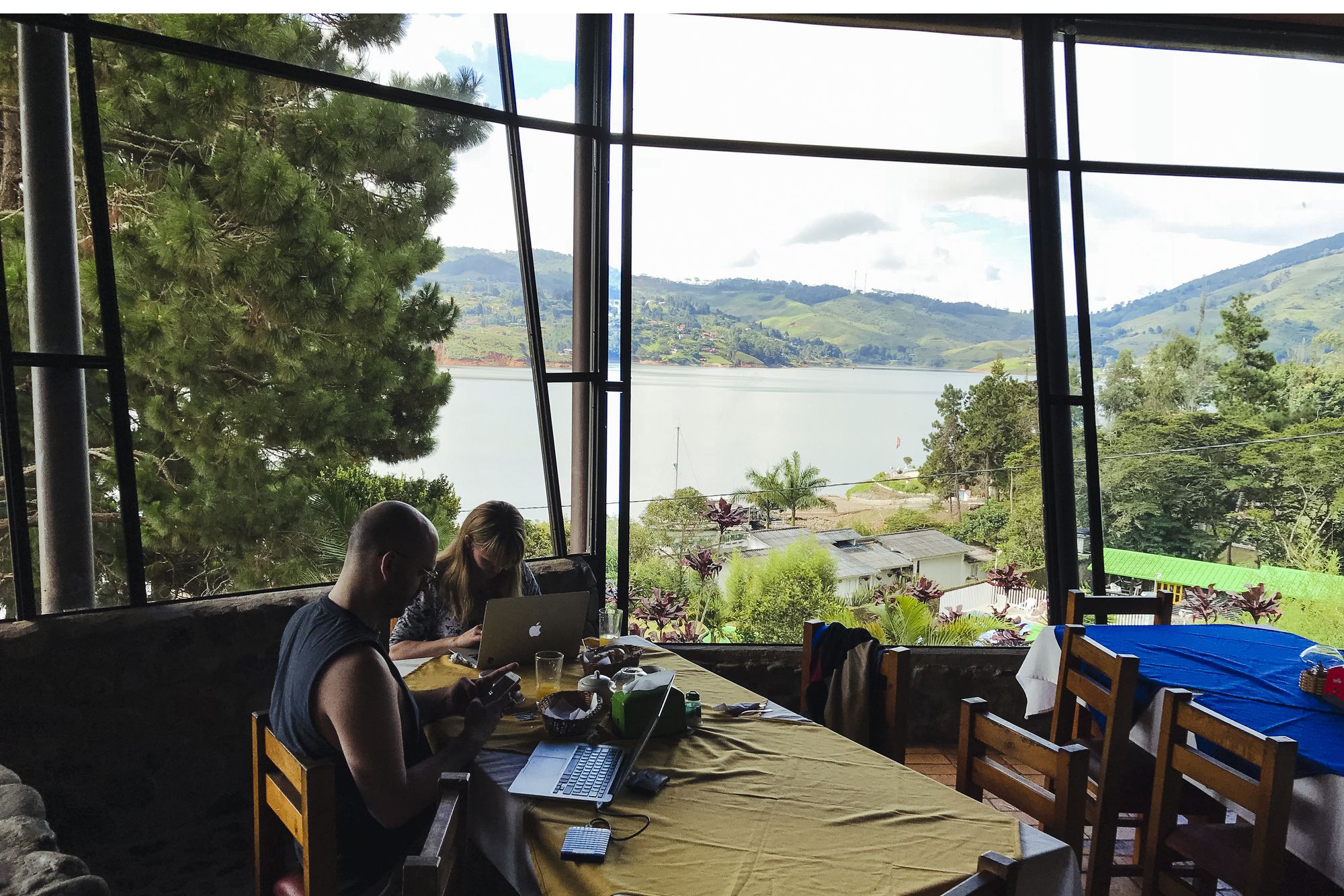 Two people on a working retreat on personal computers around the breakfast table, overlooking overlooking lake and mountains in Colombia